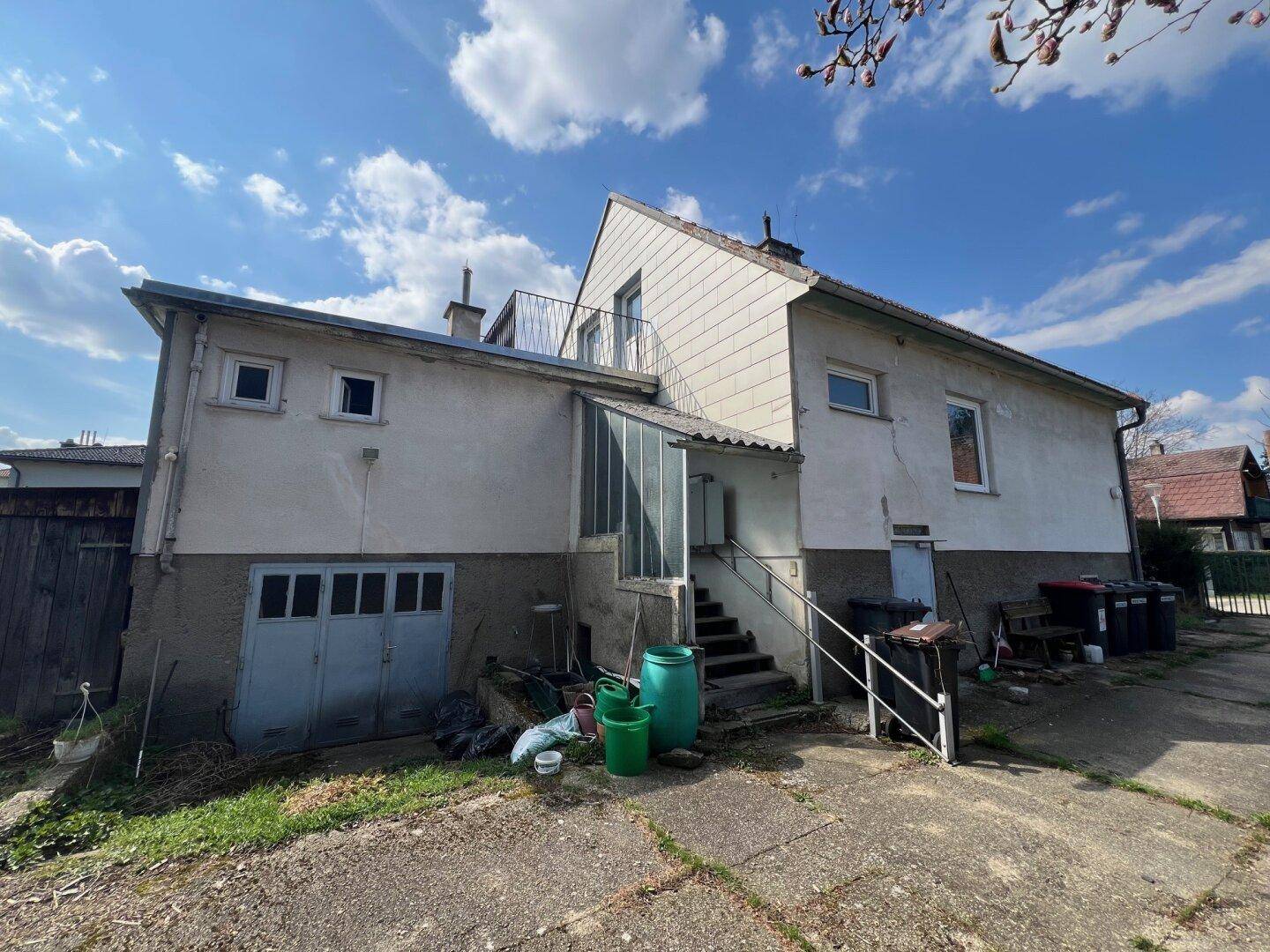 Rückseite des Hauses mit Anbau, Garage im Untergeschoss und Außentreppe zu einem oberen Bereich.