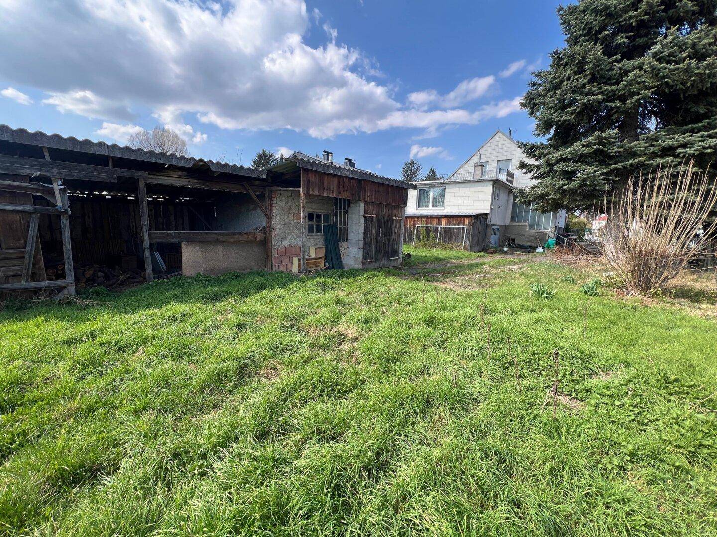Blick auf die Rückseite eines alten Schuppens und eine weitere Rasenfläche im Gartenbereich des Anwesens.
