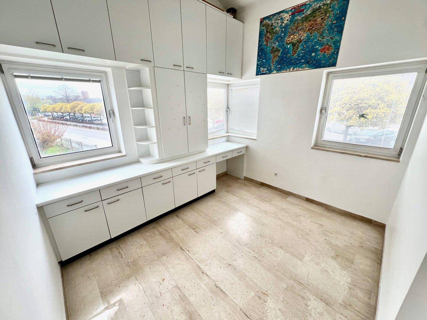 Helles Arbeitszimmer mit Einbauschränken, Schreibtisch und Blick ins Grüne durch große Fenster.
