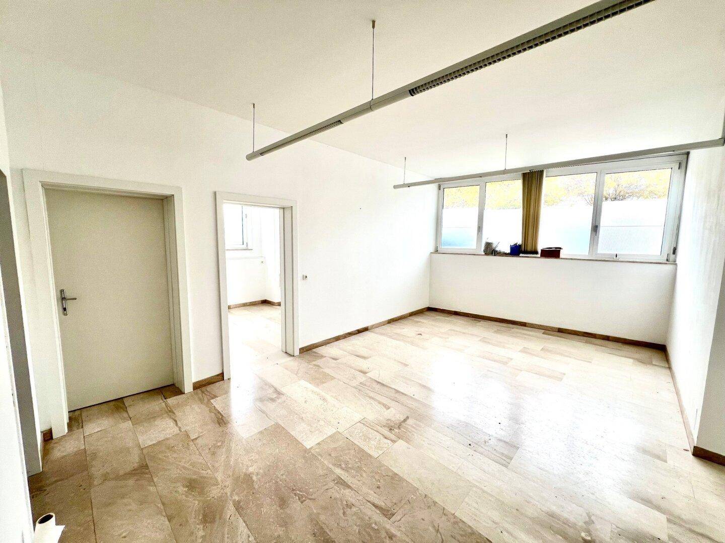 Heller, leerer Raum mit großen Fenstern und Steinboden, geeignet als Büro oder Wohnbereich.