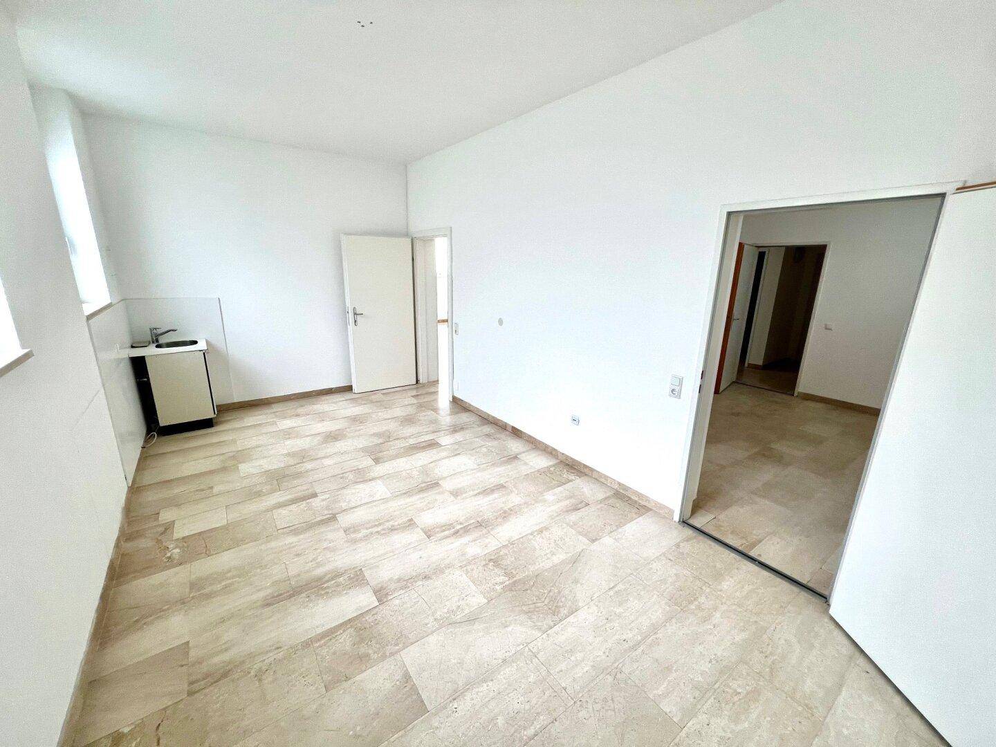 Heller Raum mit Steinboden und kleiner Küchenzeile, ideal für ein Studio oder Büro.