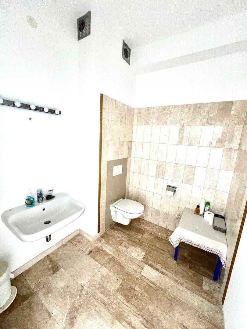 Modernes Badezimmer mit Wand-WC, Waschbecken und hellen Fliesen an Wänden und Boden.