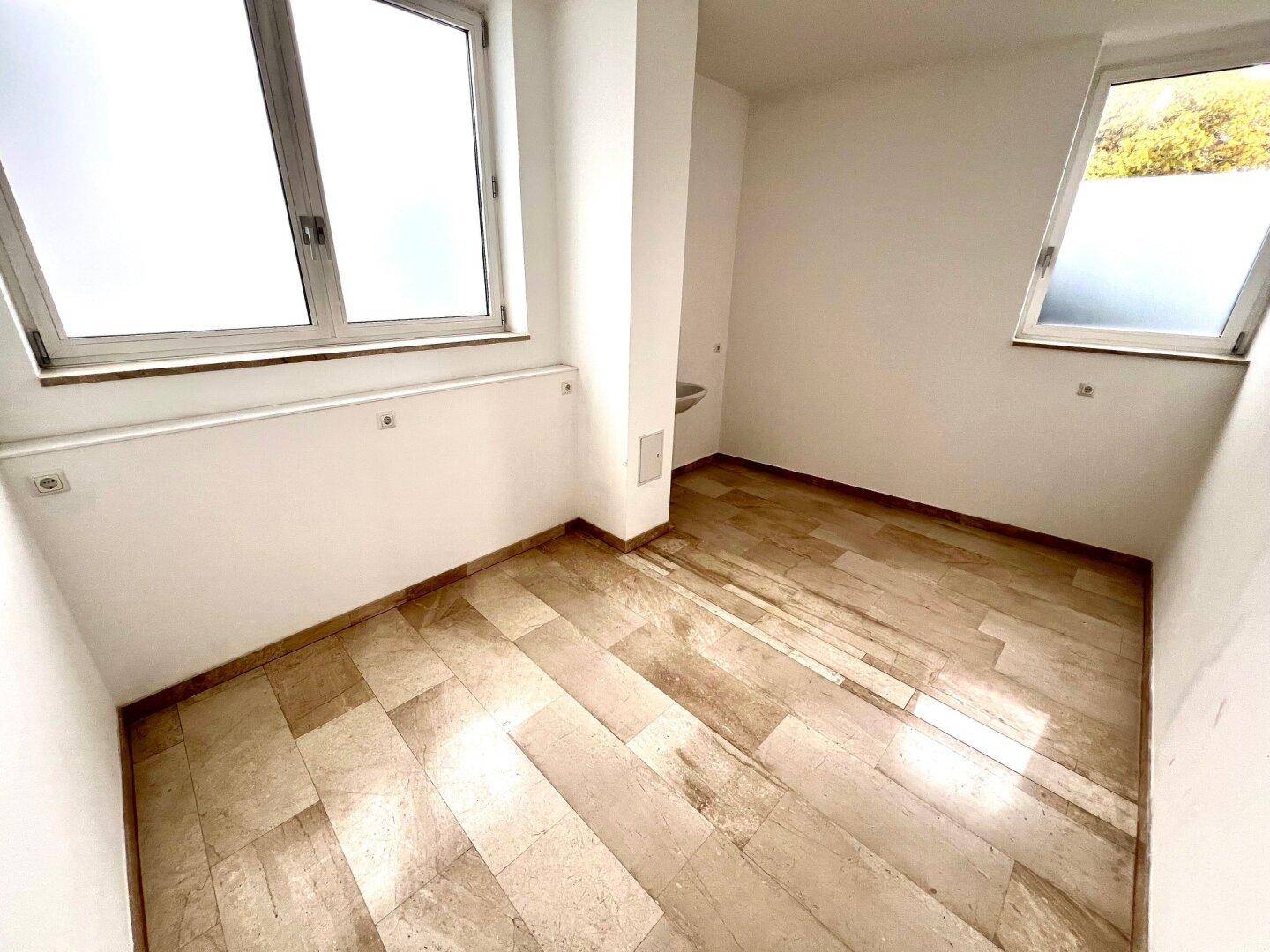 Kleiner, heller Raum mit zwei Fenstern und Steinboden, vielseitig nutzbar.