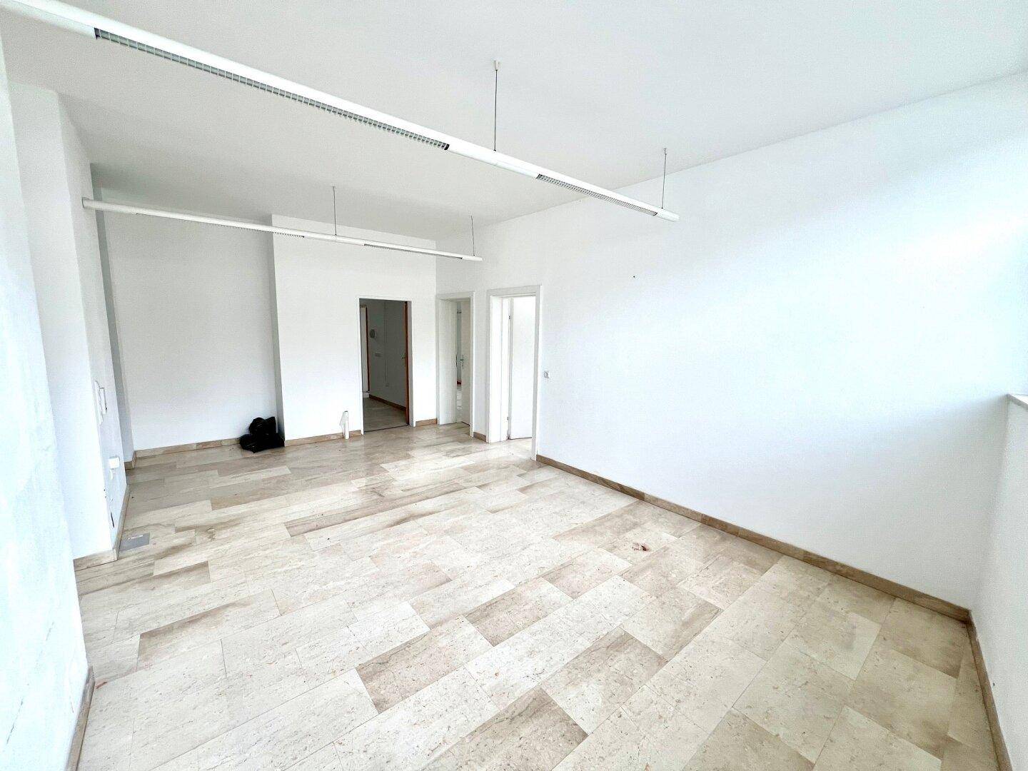 Geräumiger, heller Raum mit Steinboden und großen Fenstern, ideal als Bürofläche.