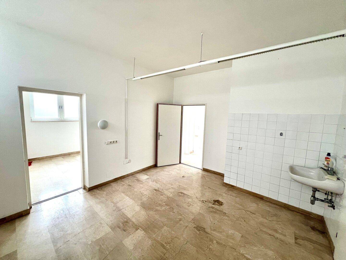 Heller Raum mit Steinboden, gefliester Wand und Waschbecken, vielseitig nutzbar.
