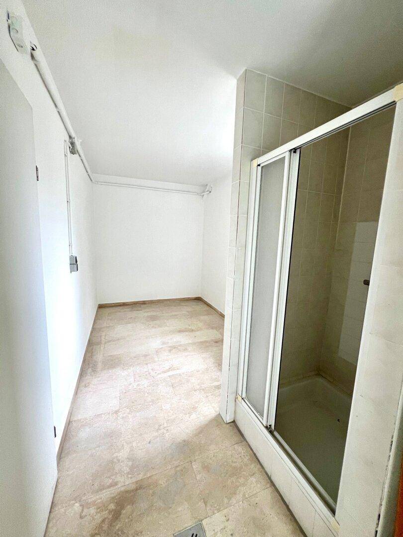 Einfaches Badezimmer mit Duschkabine und Steinboden, funktional und hell.