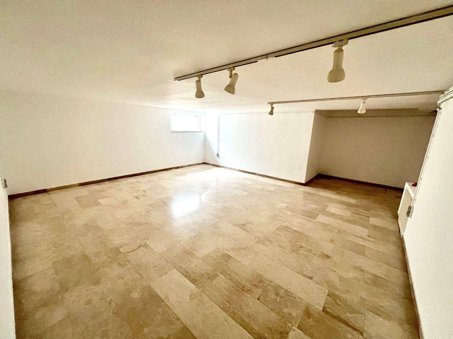 Großer Kellerraum mit Steinboden, Schienenbeleuchtung und natürlichem Lichteinfall.