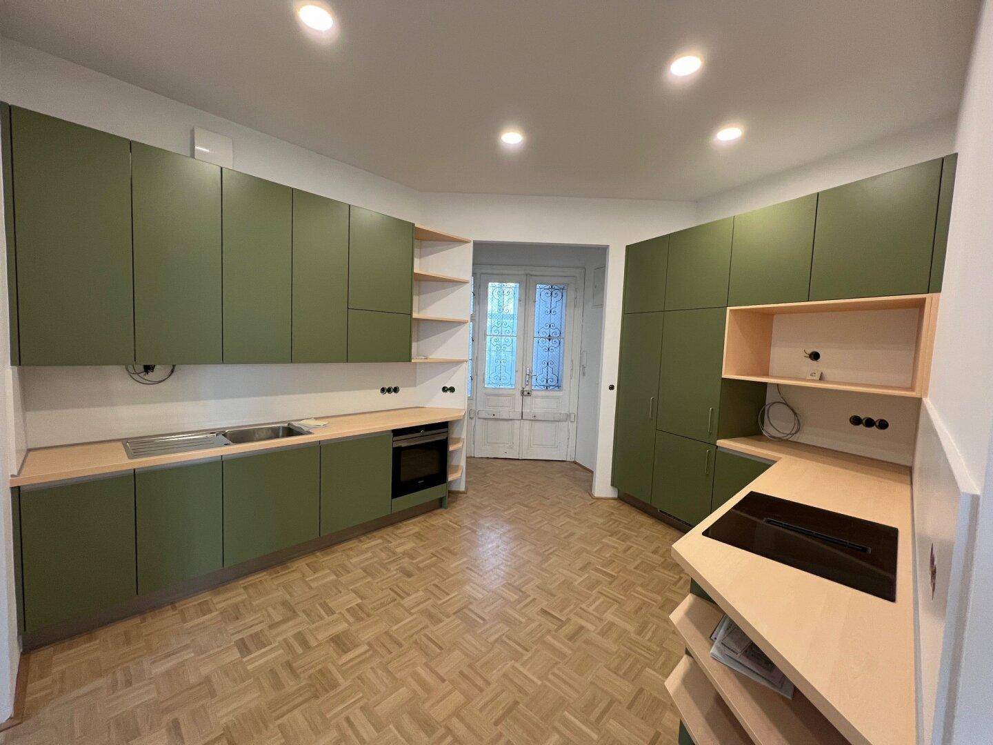 Moderne Küche mit grünen Schränken, Holzarbeitsplatten und integrierten Kochfeldern und Backofen.