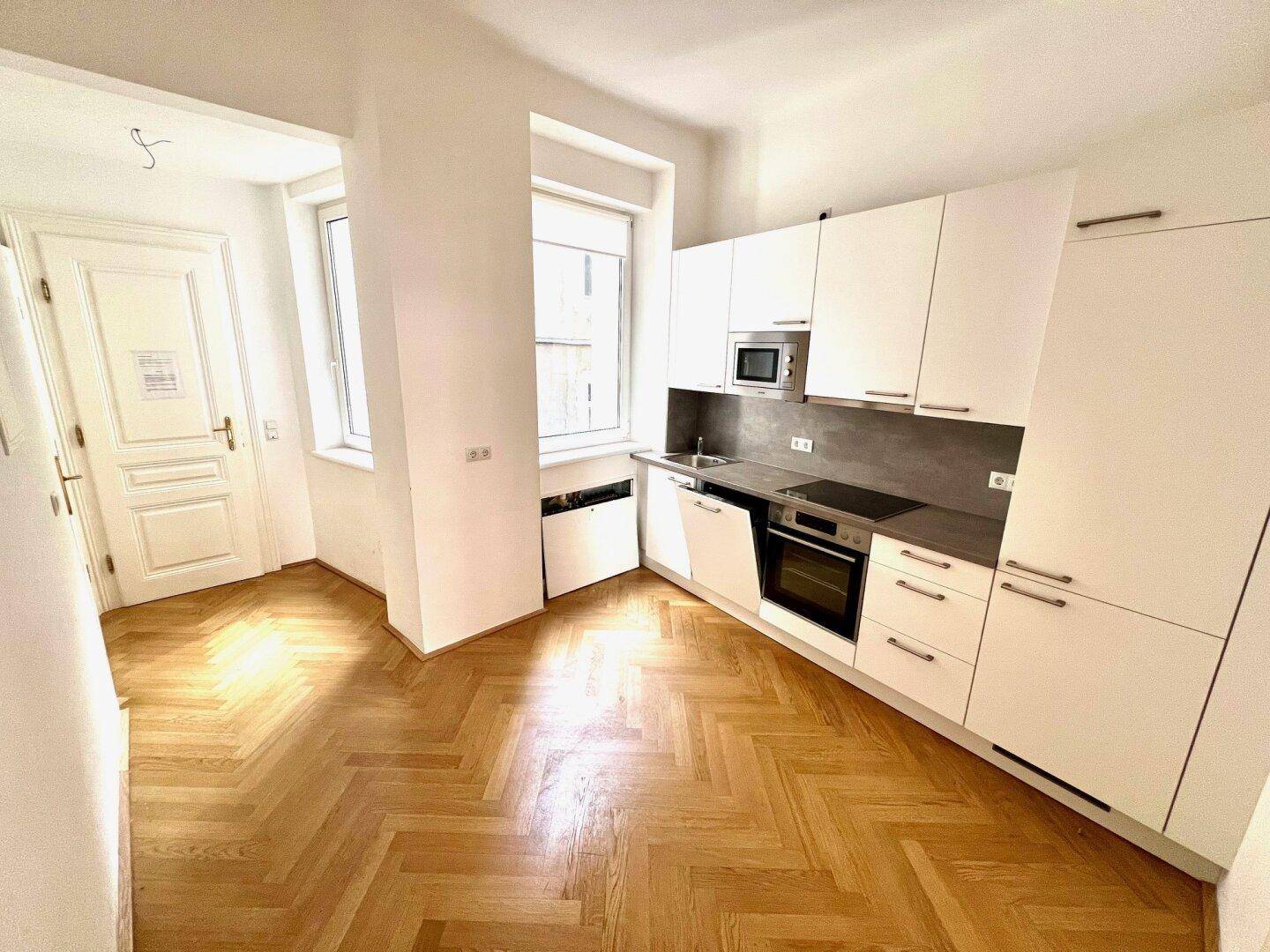 Moderne Einbauküche mit weißen Schränken, integrierten Geräten und Fischgrätparkettboden.