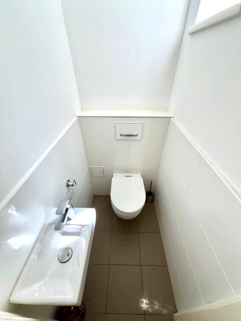 Kleines Gäste-WC mit wandhängendem WC, Handwaschbecken und hellen Fliesen.