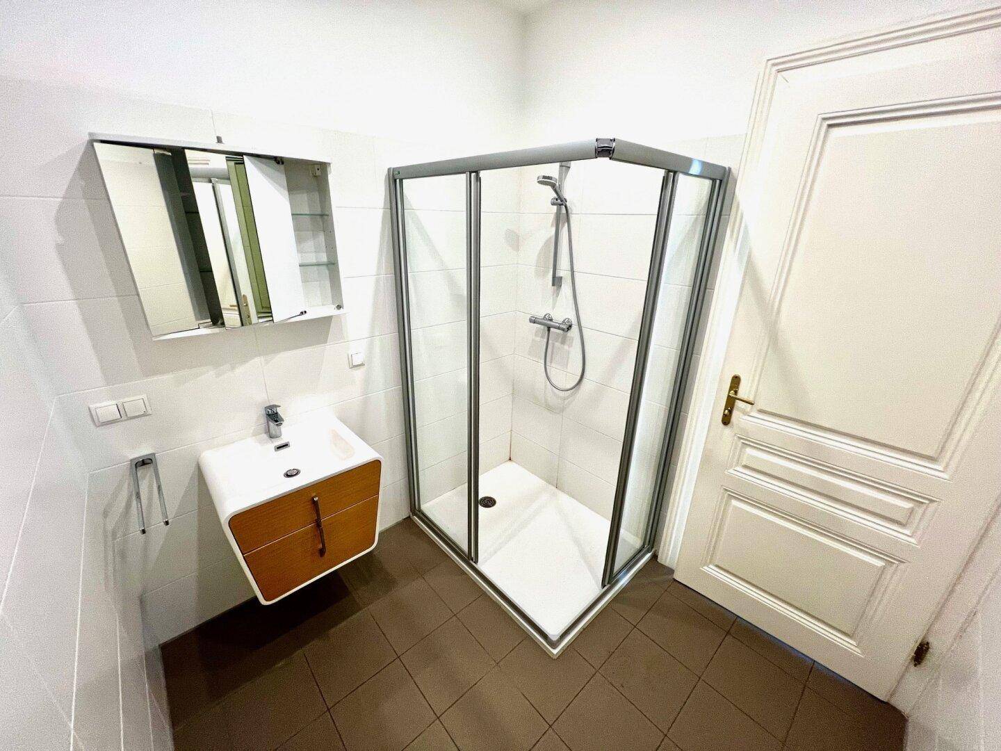 Modernes Badezimmer mit Duschkabine, Waschtisch und Spiegelschrank, hell gefliest.
