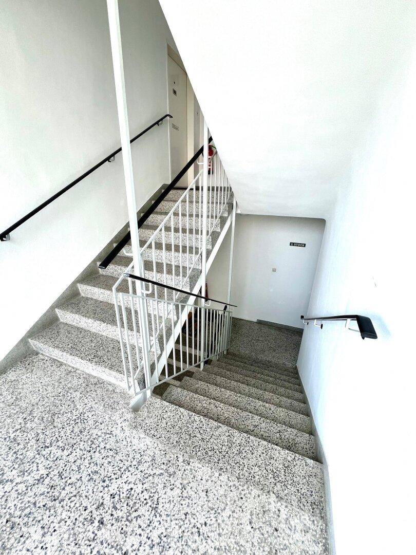 Treppenhaus mit Terrazzoboden und weißen Geländern, das mehrere Stockwerke verbindet.