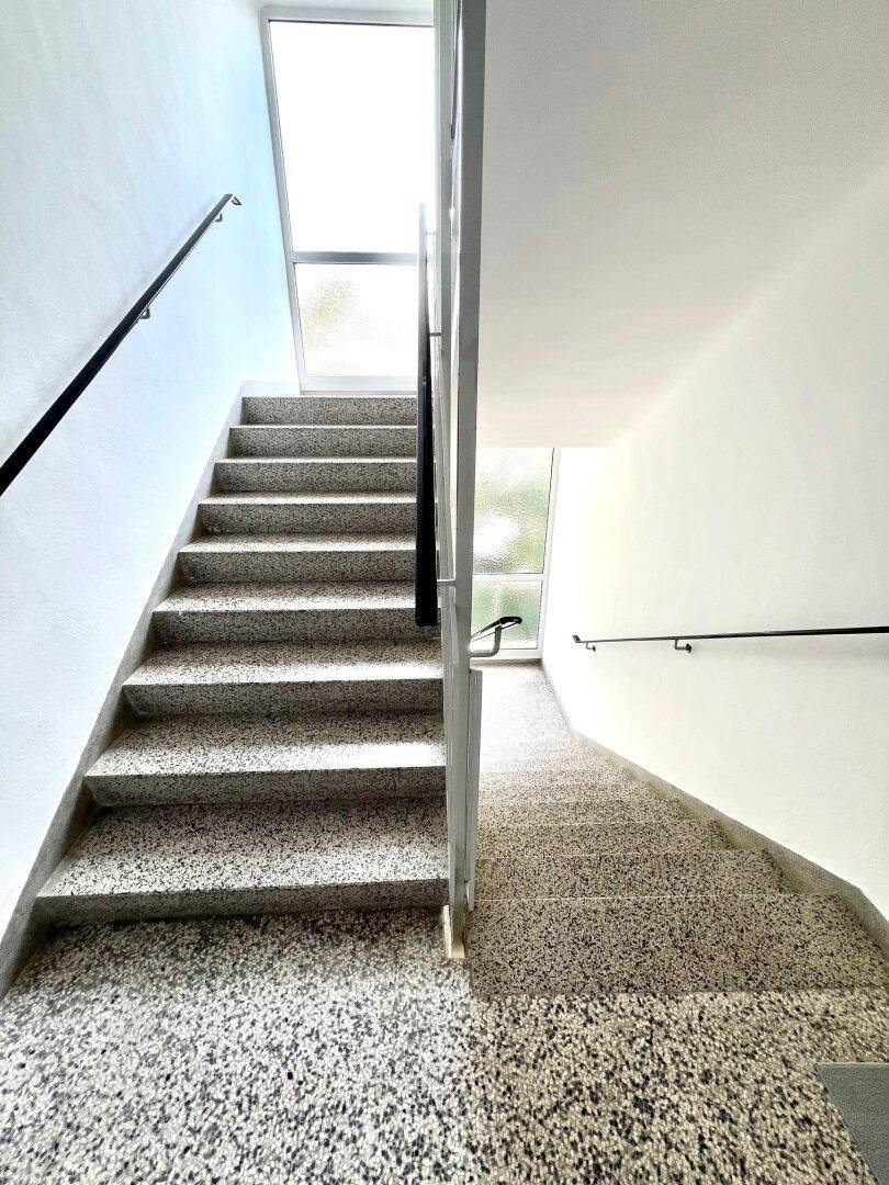 Helles Treppenhaus mit Terrazzostufen und Fenster für natürliches Licht.