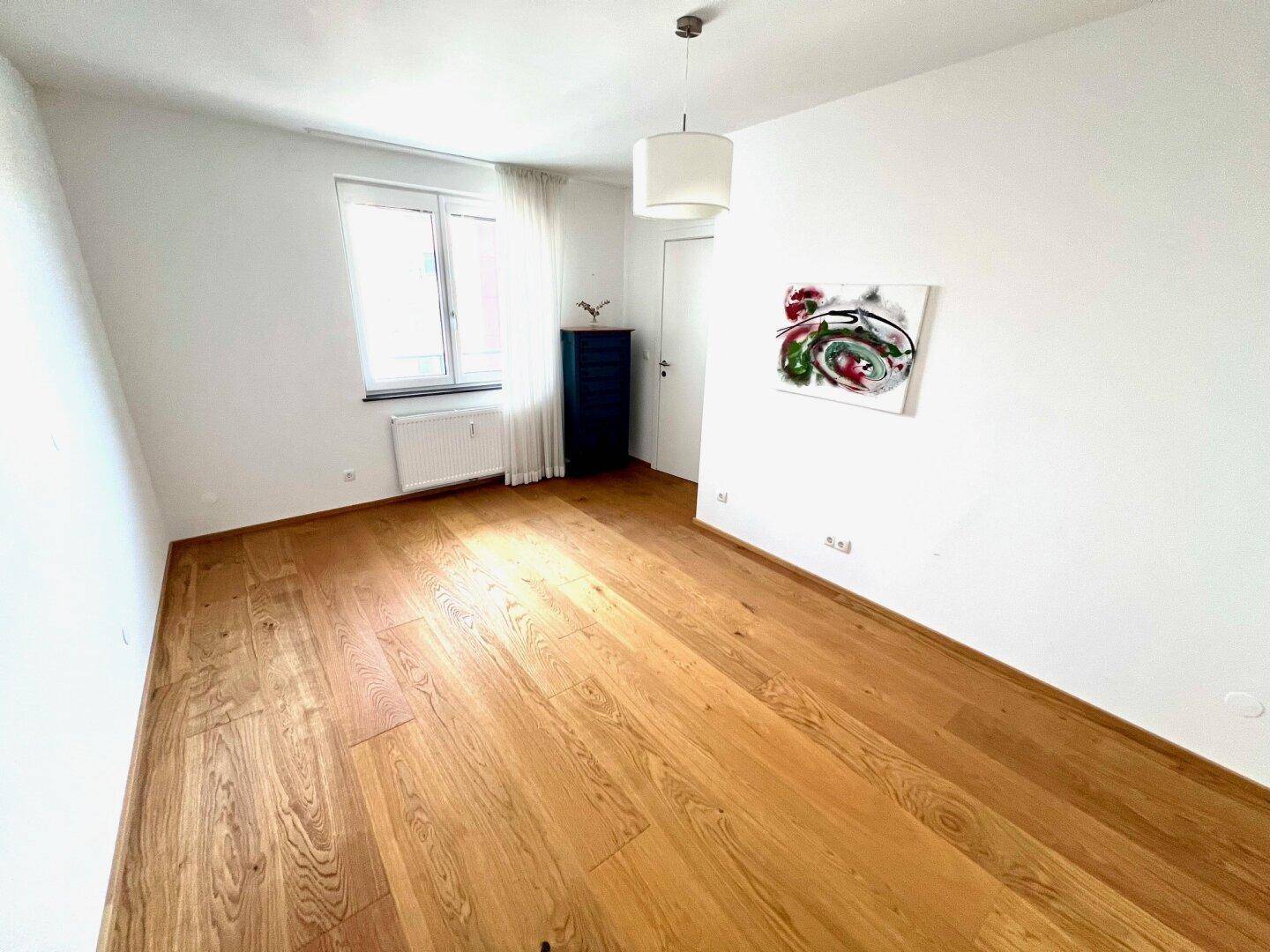 Helles Zimmer mit Holzboden und großem Fenster, ideal als Schlaf- oder Arbeitszimmer nutzbar.