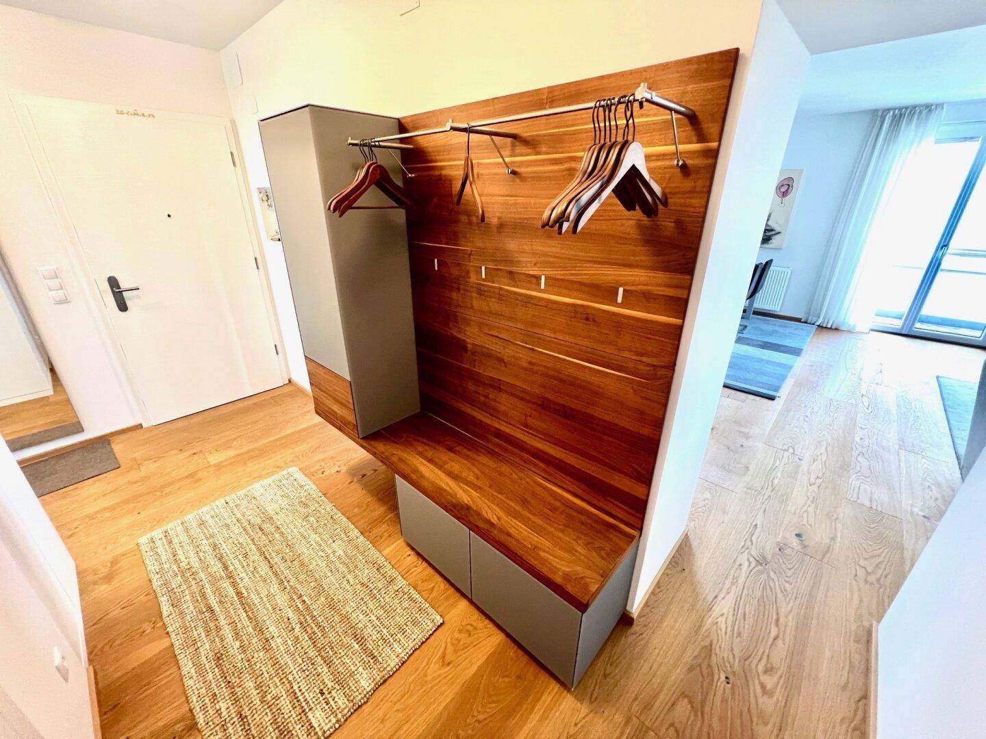 Heller Eingangsbereich mit moderner Garderobe aus Holz und praktischer Sitzbank auf Holzboden.