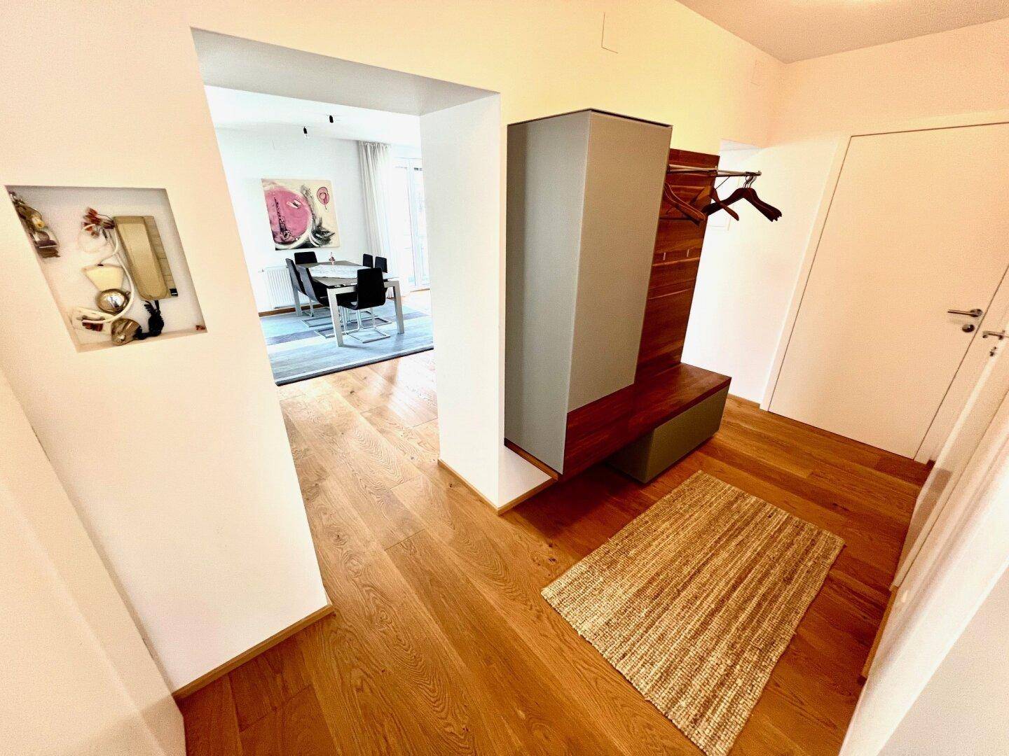 Heller Eingangsbereich mit Holzboden und Garderobe, der in einen Essbereich übergeht.