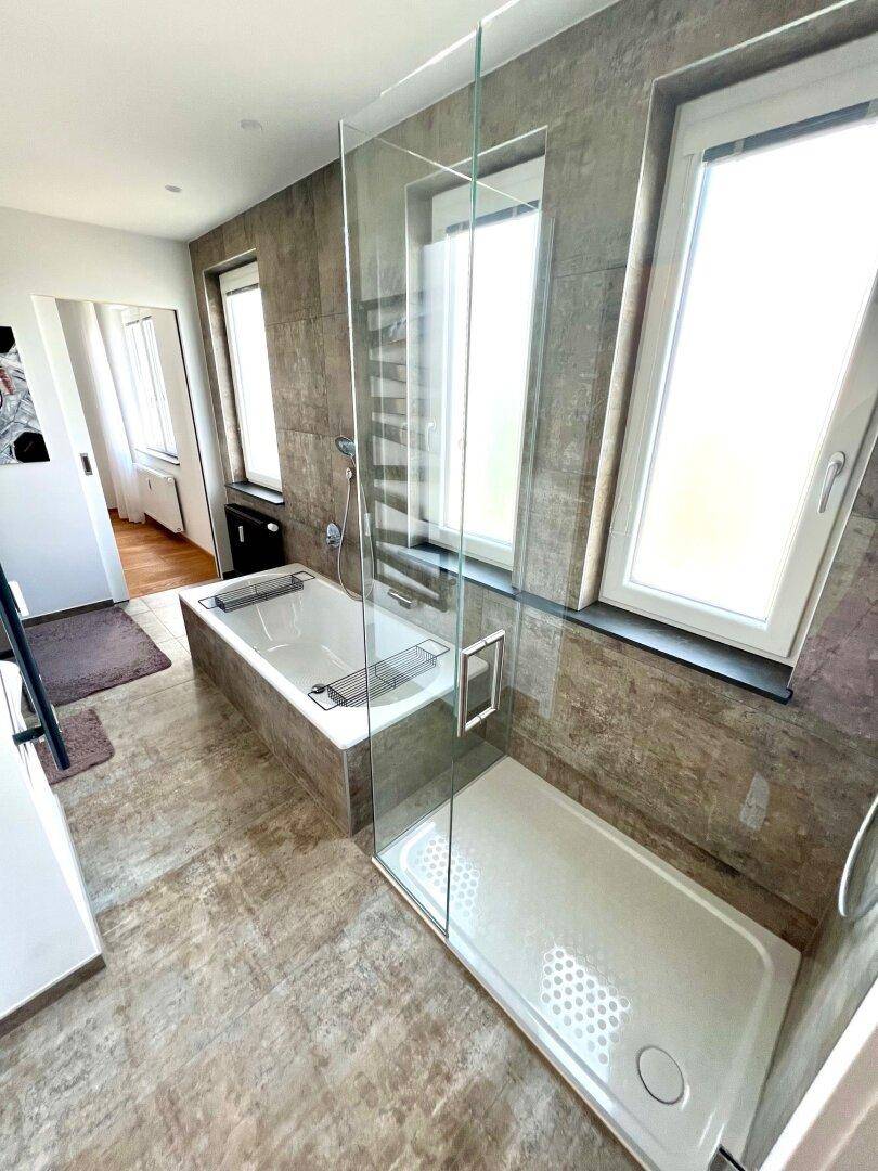 Geräumiges Badezimmer mit moderner Duschkabine, Badewanne und großen Fenstern für Tageslicht.