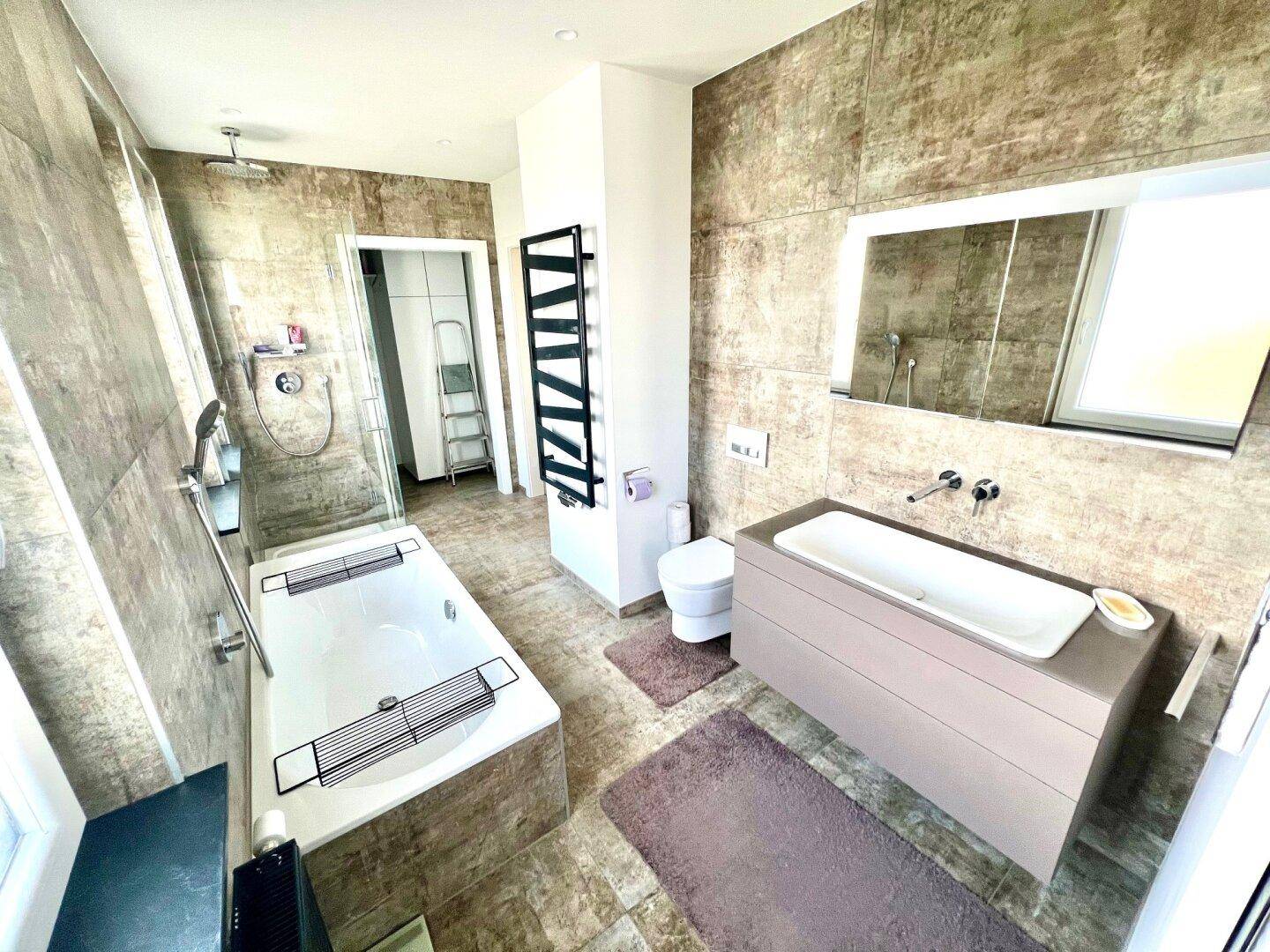 Modernes Badezimmer mit großformatigen Fliesen, Badewanne, Dusche und beheiztem Handtuchhalter.