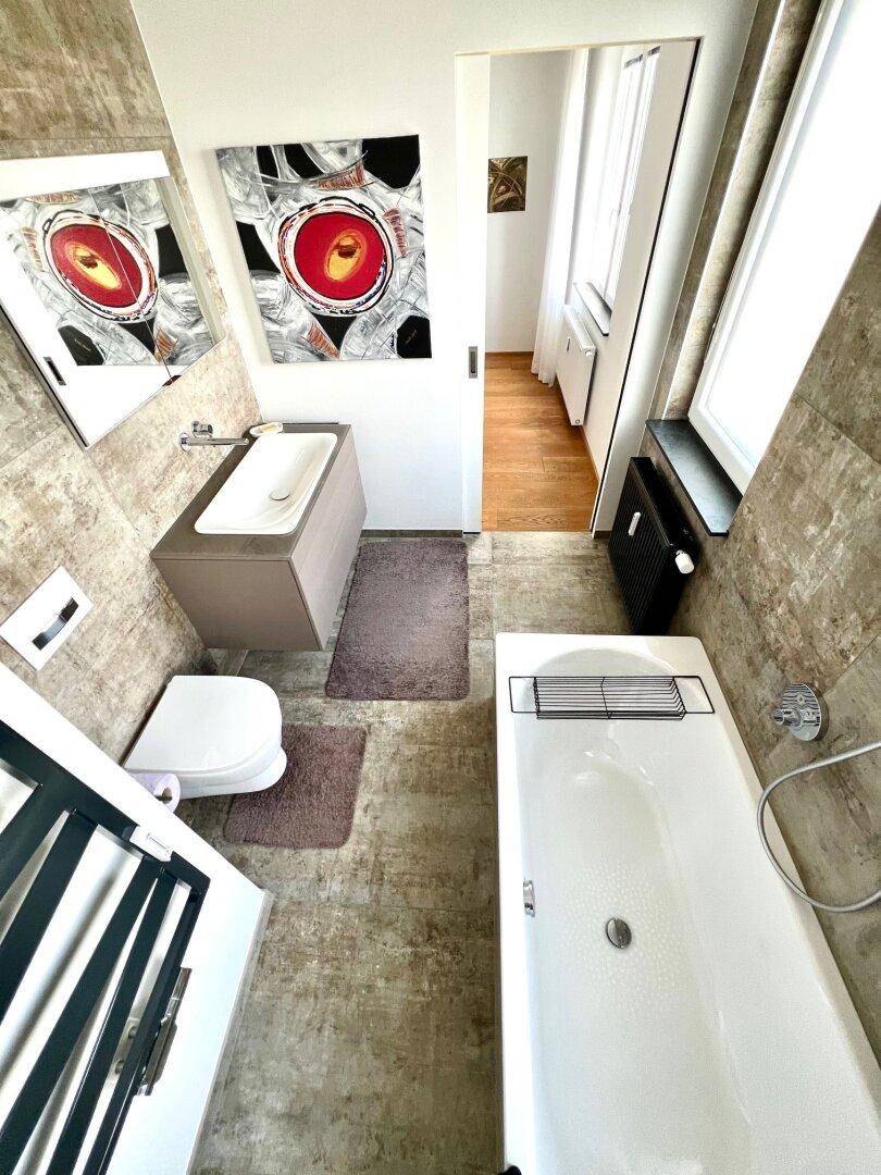 Stilvolles Badezimmer mit Waschtisch, WC, Badewanne und Blick in das angrenzende Schlafzimmer.
