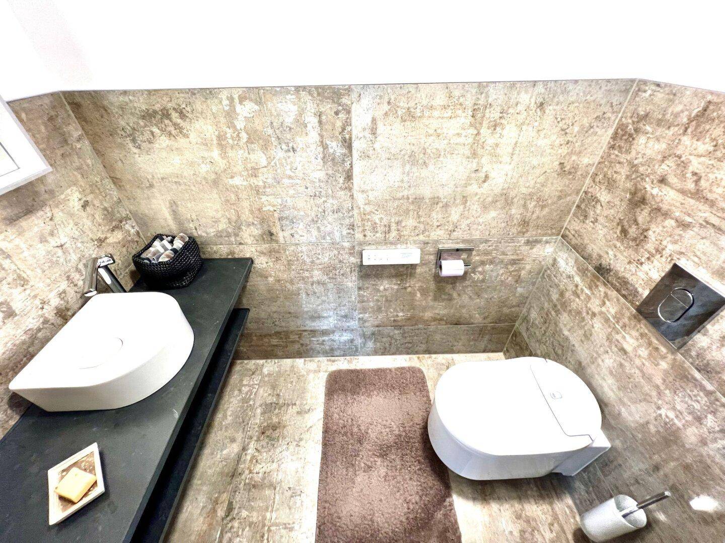 Modernes Gäste-WC mit stilvollem Waschtisch und wandhängender Toilette in Fliesenoptik.