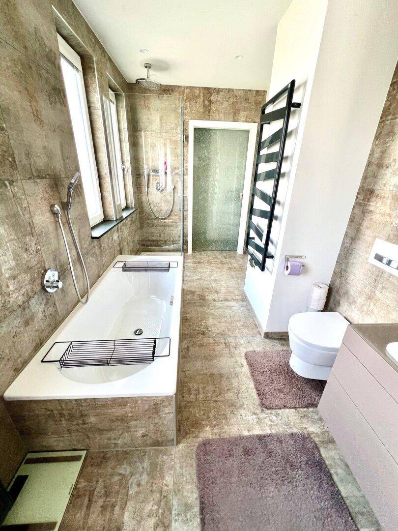 Elegantes Badezimmer mit Badewanne, Dusche, WC und modernem beheiztem Handtuchhalter.