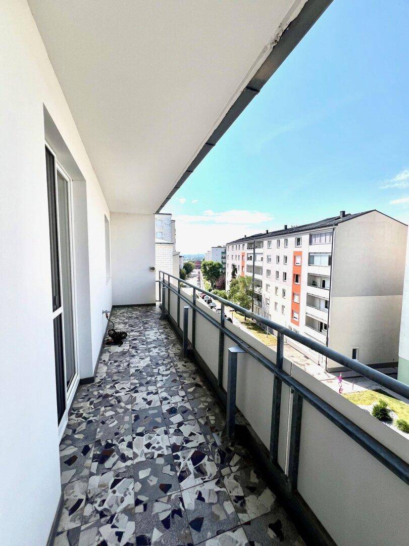 Langer Balkon mit Fliesenboden und Blick auf die umliegenden Gebäude und die Stadtlandschaft.