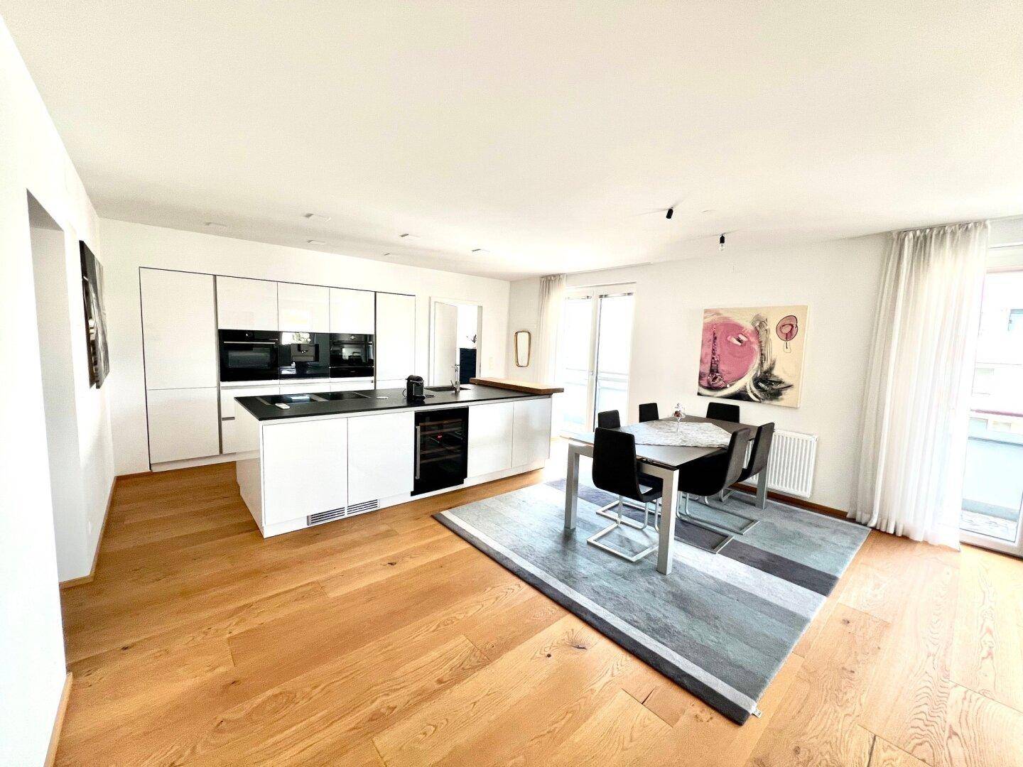 Moderne weiße Einbauküche mit Essbereich und Zugang zum Balkon, hell und offen gestaltet.