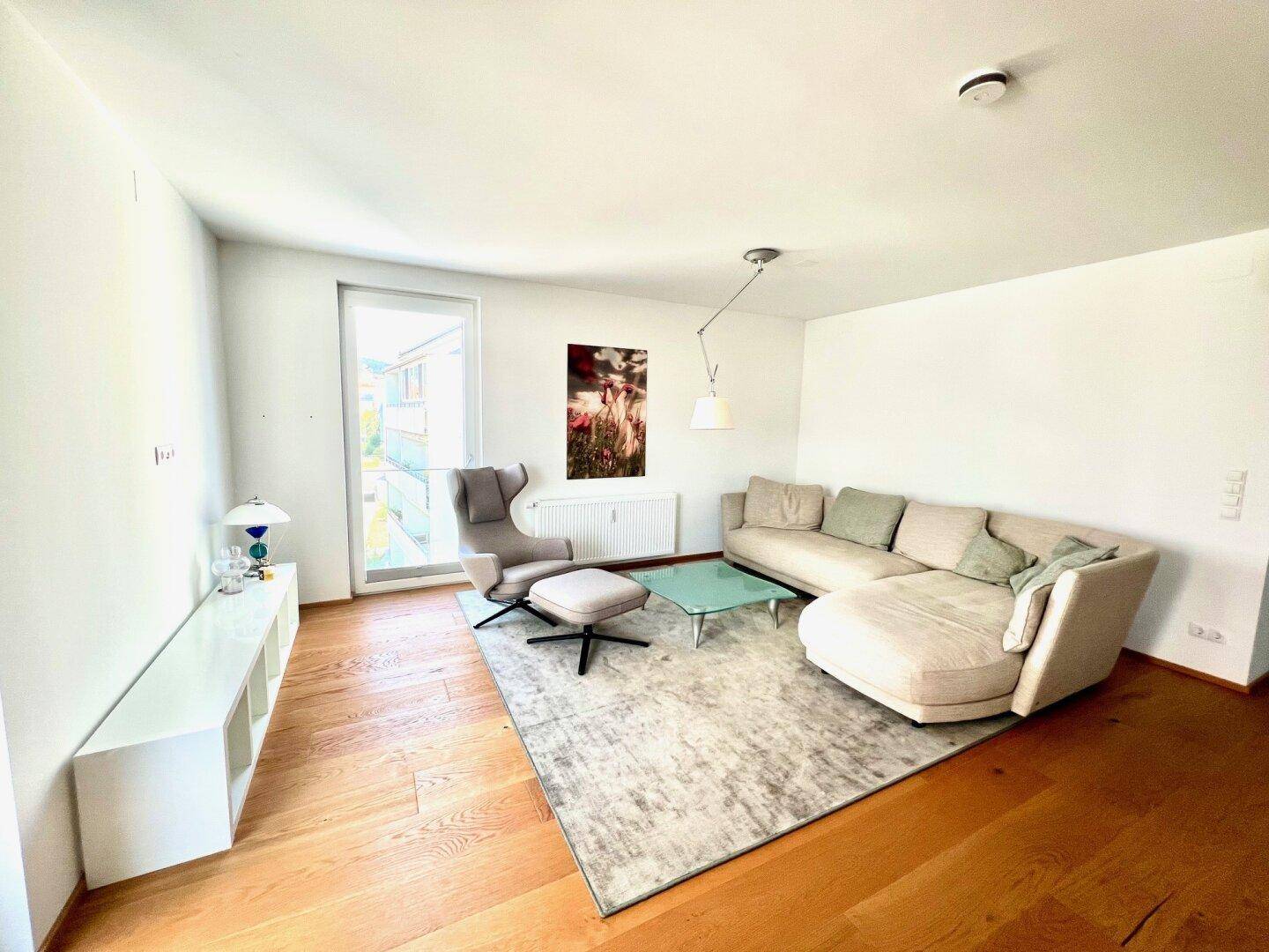 Geräumiges Wohnzimmer mit modernem Sofa, Sessel und großem Fenster für viel natürliches Licht.