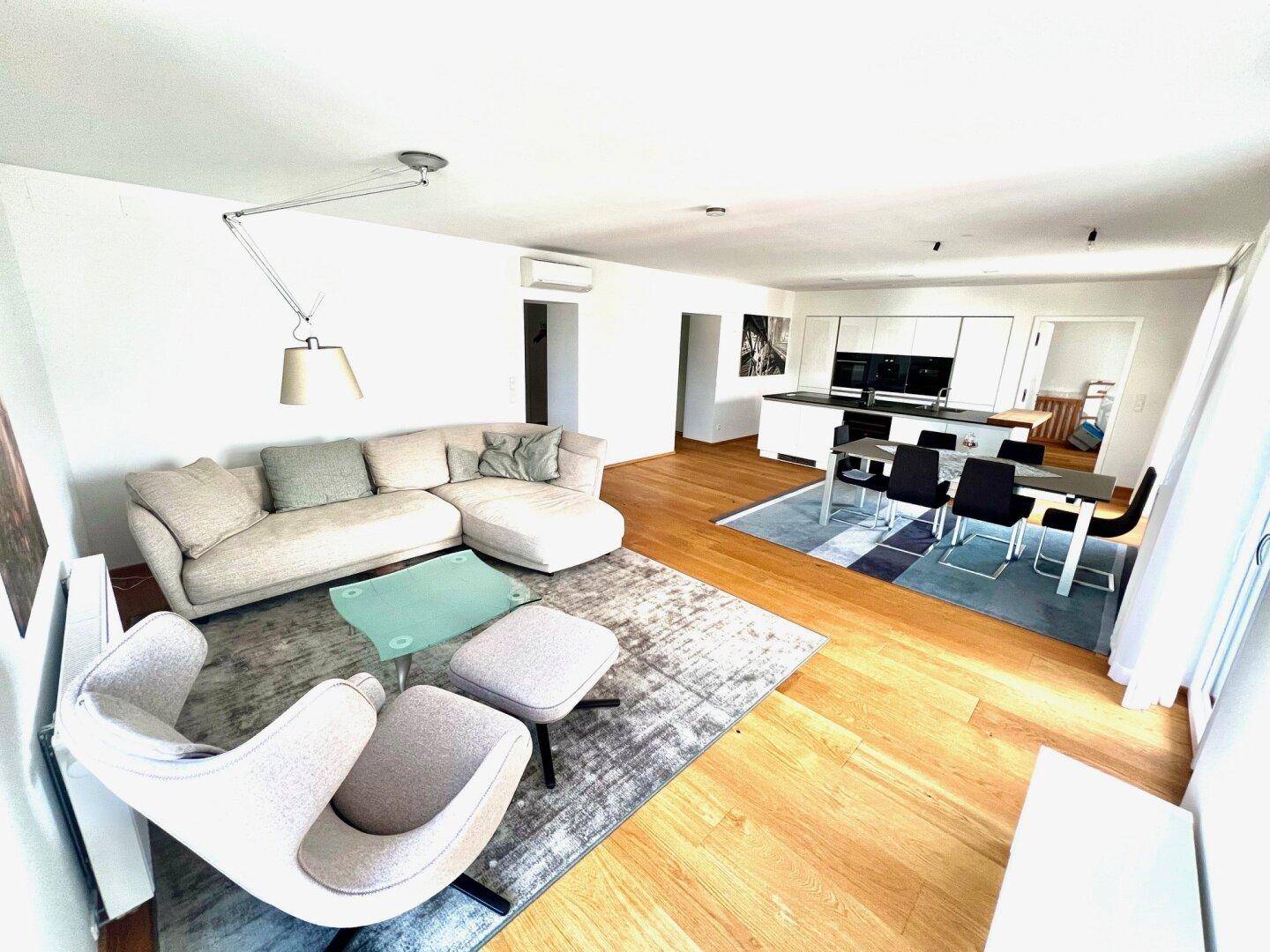 Gemütlicher Wohnbereich mit Sofa und Blick auf den modernen Ess- und Küchenbereich mit Holzboden.
