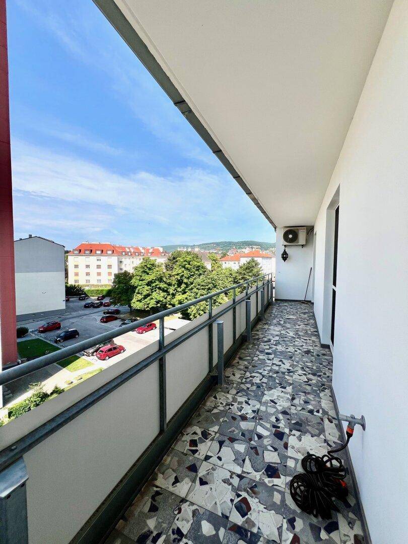 Geräumiger Balkon mit Fliesenboden, Blick auf die Stadt und eine Klimaanlage an der Wand.
