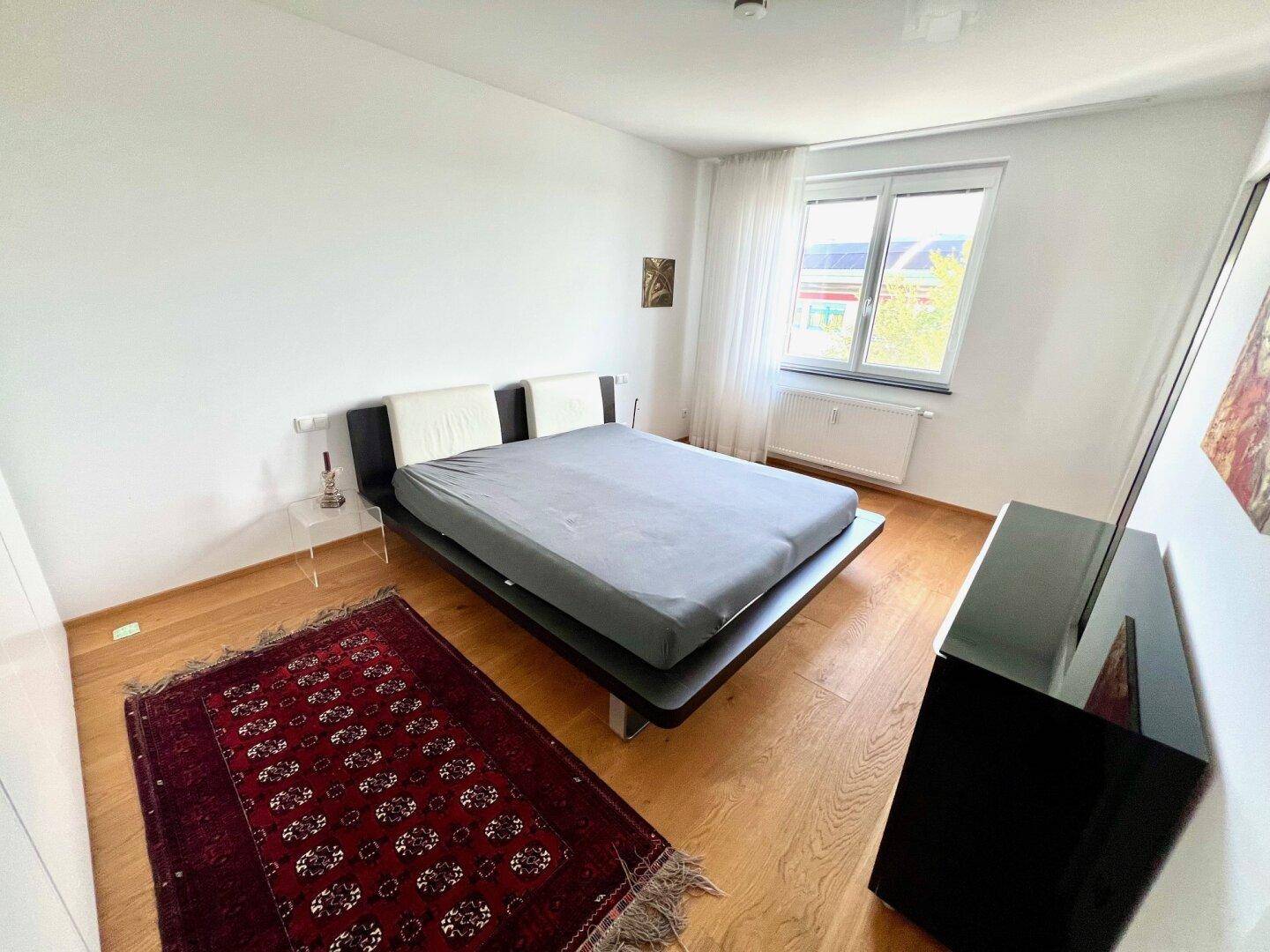 Modernes Schlafzimmer mit Holzboden, großem Bett und Fenster für natürliche Belichtung.