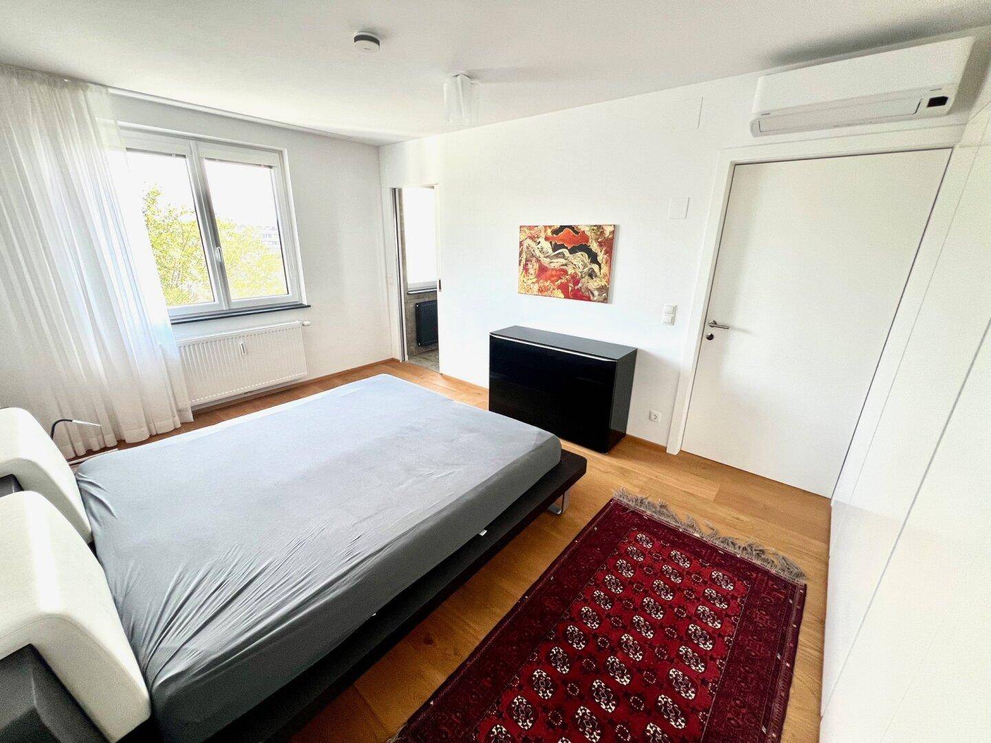 Komfortables Schlafzimmer mit Holzboden, Klimaanlage und Blick nach draußen durch das Fenster.