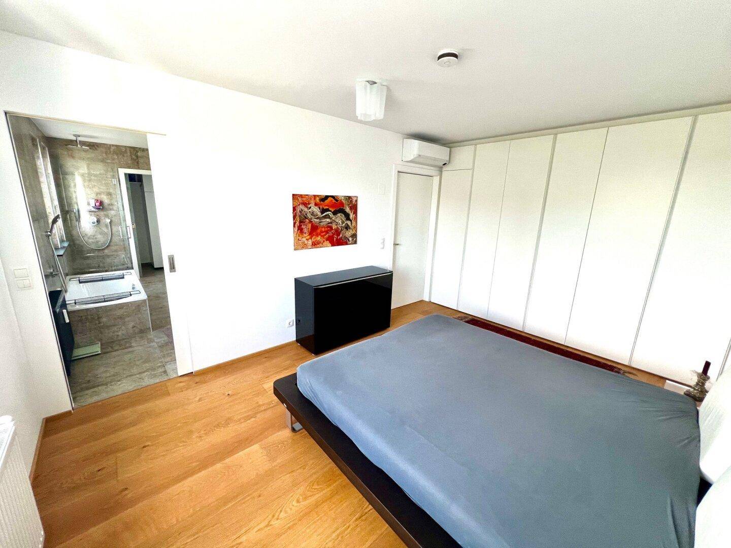 Schlafzimmer mit Holzboden, Einbauschränken und direktem Zugang zum modernen Badezimmer.