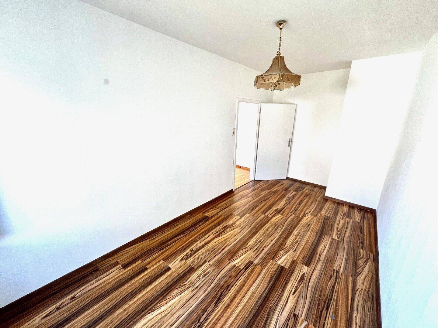 Leeres Zimmer mit markantem Laminatboden und einer Doppeltür, die zu einem weiteren Raum führt.