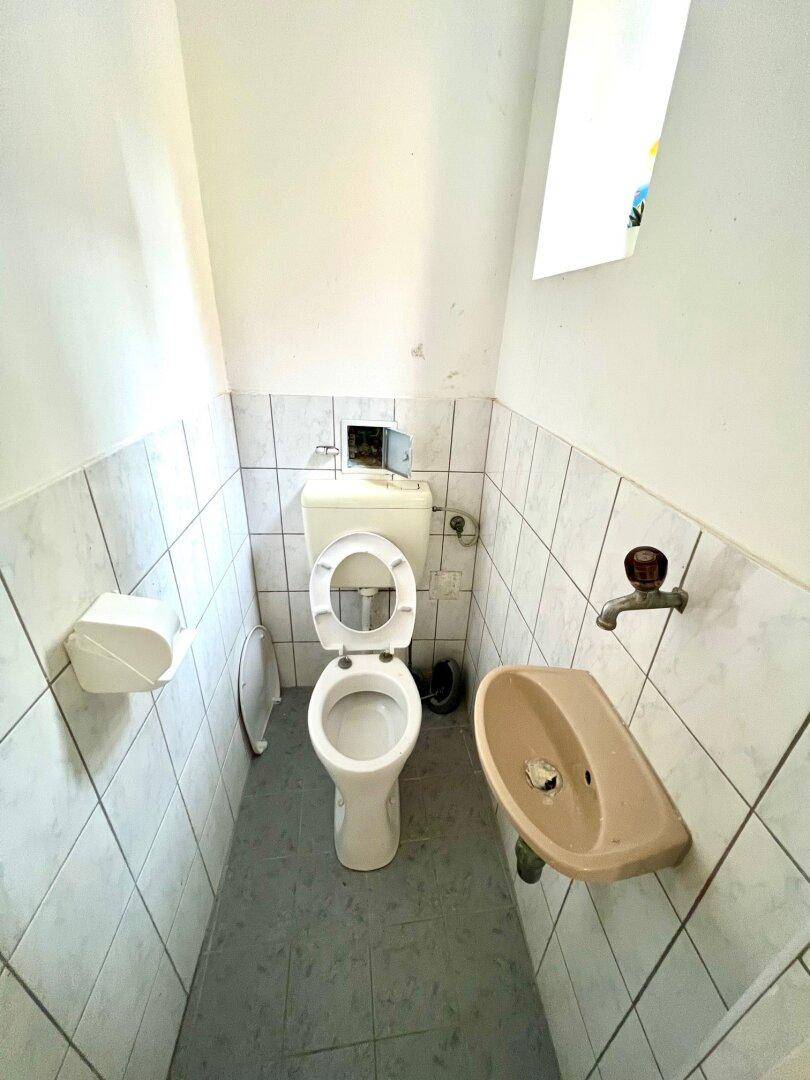 Separates WC mit Toilette und kleinem Handwaschbecken, hell gefliest und funktional eingerichtet.