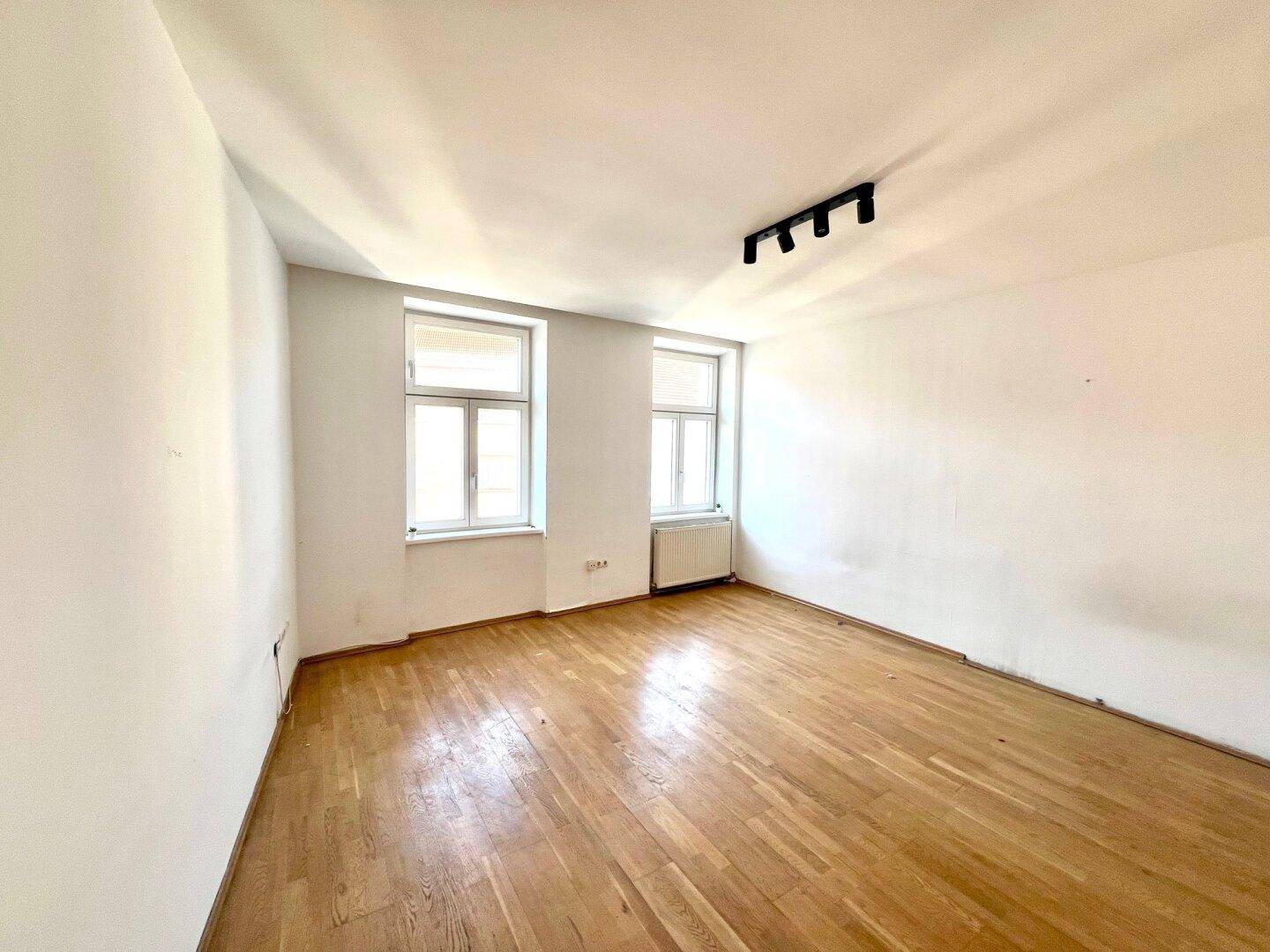 Geräumiges Zimmer mit klassischem Holzparkett und viel Tageslicht durch die großen Fenster.