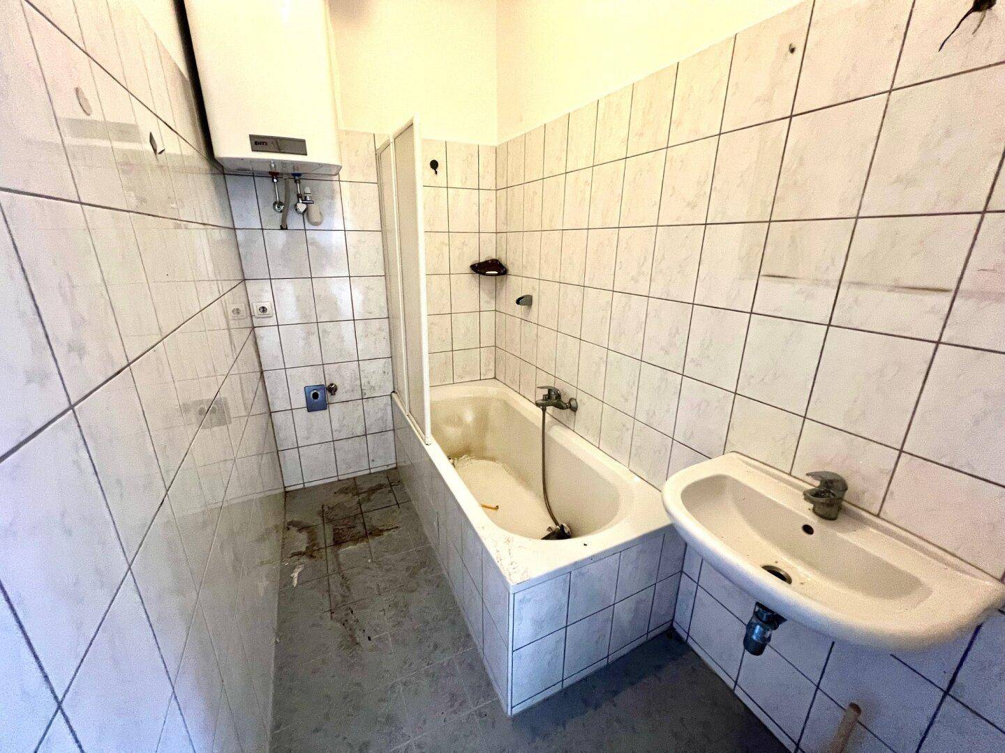 Gefliestes Badezimmer mit Badewanne, Duschvorhang und Waschbecken, ausgestattet mit einem Warmwasserboiler.