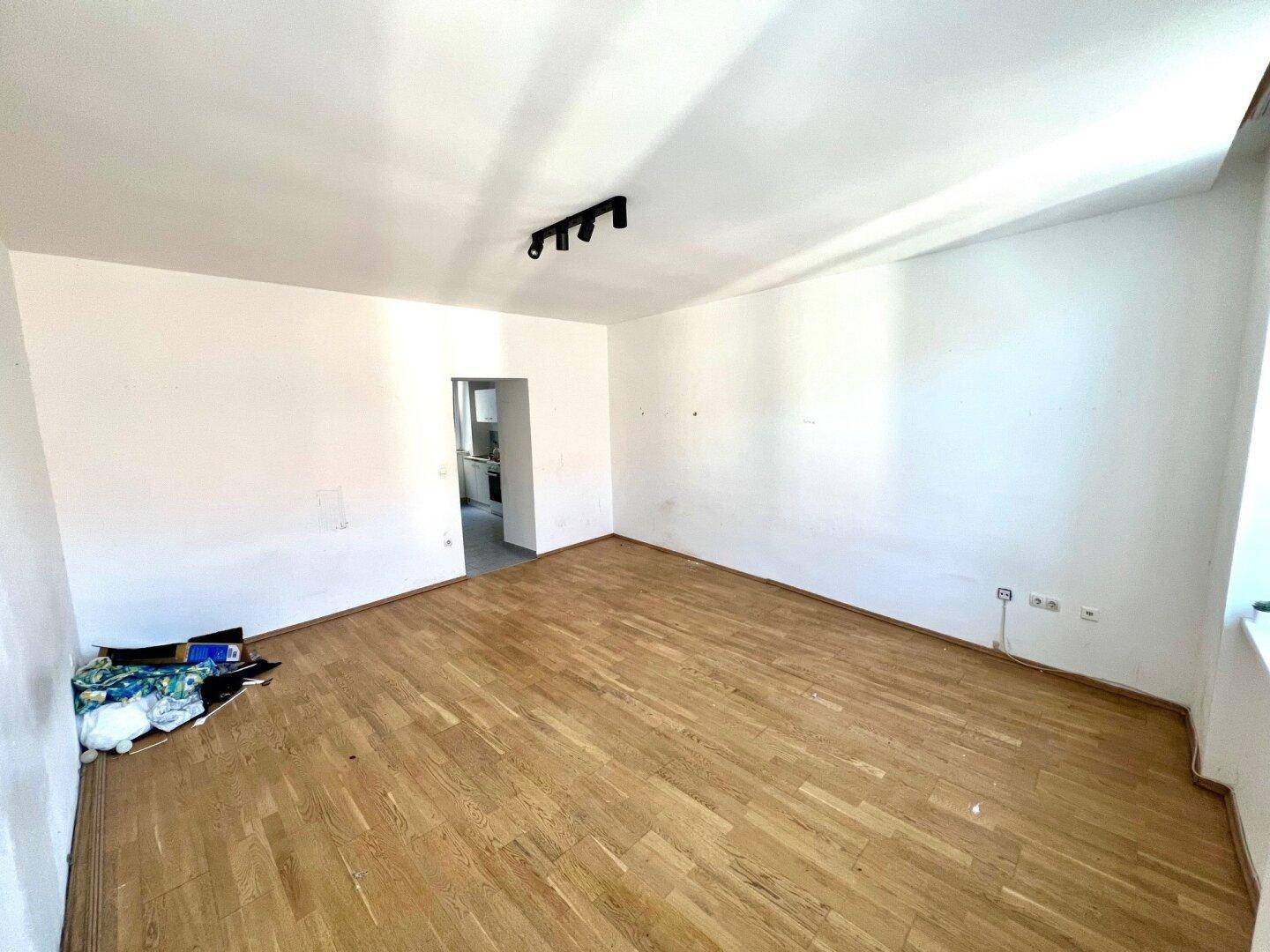 Heller Wohnbereich mit Holzparkett und offenem Zugang zu einem weiteren Raum.