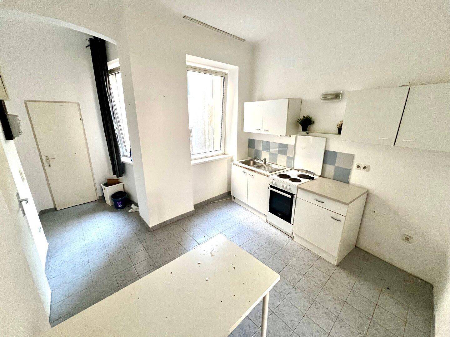 Funktionale Küche mit Fenster, weißen Schränken und blauen Fliesen, bietet Platz für einen kleinen Tisch.