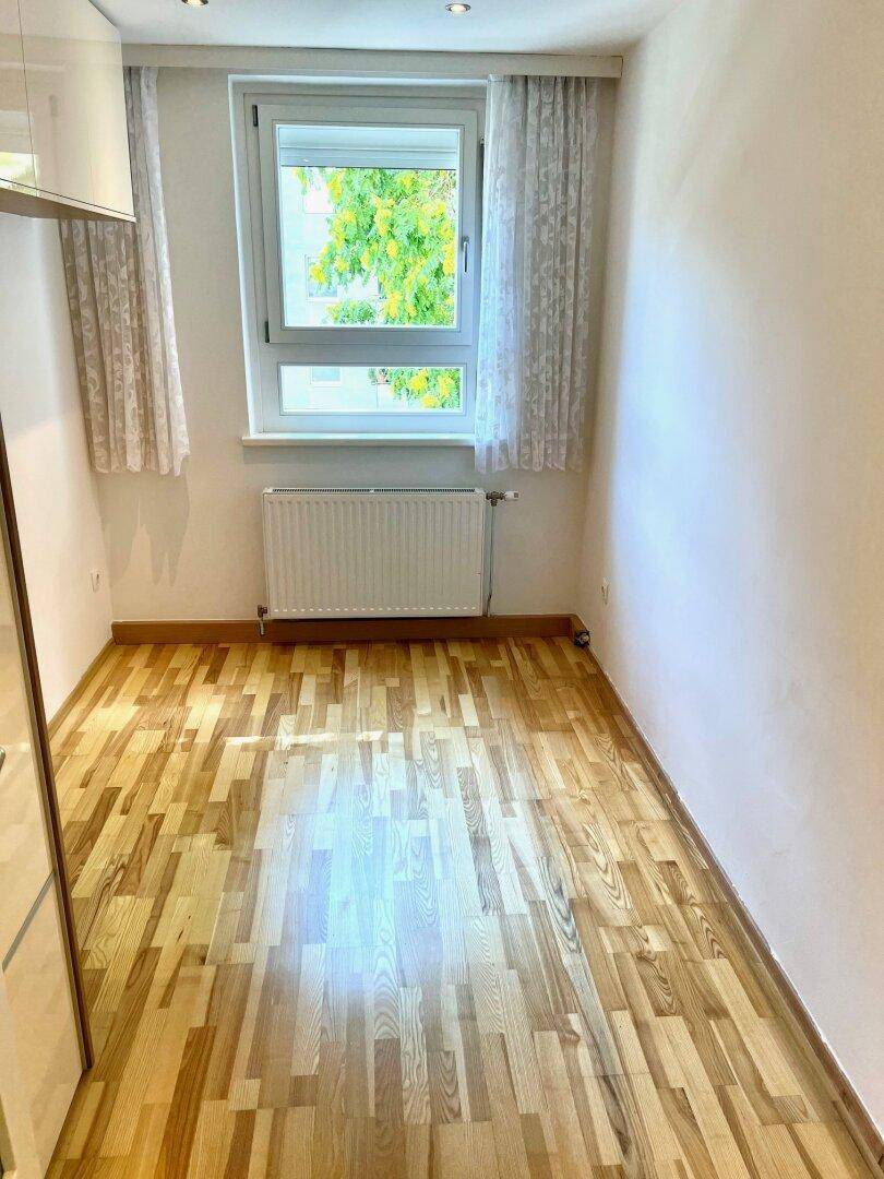 Helles Schlafzimmer mit Parkettboden, großem Fenster und Heizkörper, bietet eine angenehme Wohnatmosphäre.