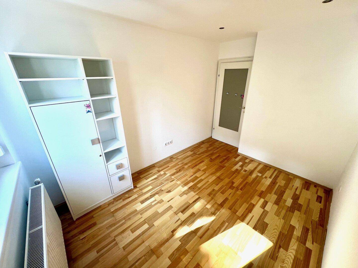 Helles Zimmer mit Parkettboden und einem weißen Regal, ideal als Kinderzimmer oder Arbeitszimmer nutzbar.