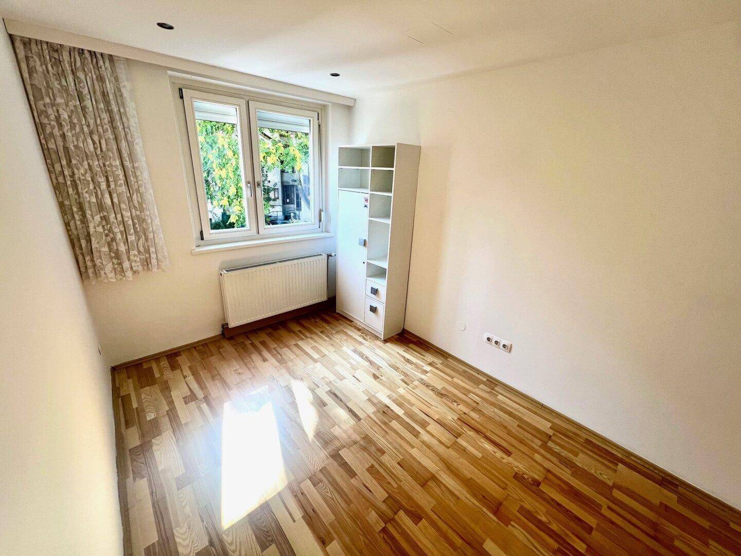Freundliches Zimmer mit Parkettboden, großem Fenster und Heizkörper, bietet viel Tageslicht.