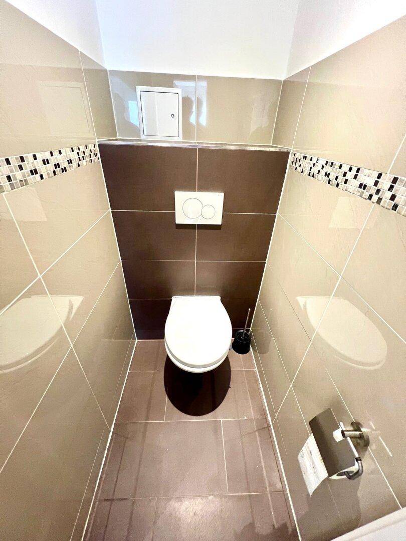 Separates WC mit wandhängender Toilette und modernen Fliesen in Braun- und Beigetönen.