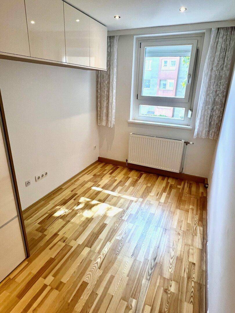 Geräumiges Schlafzimmer mit Parkettboden, Fenster mit Blick ins Grüne und praktischen Einbauschränken.