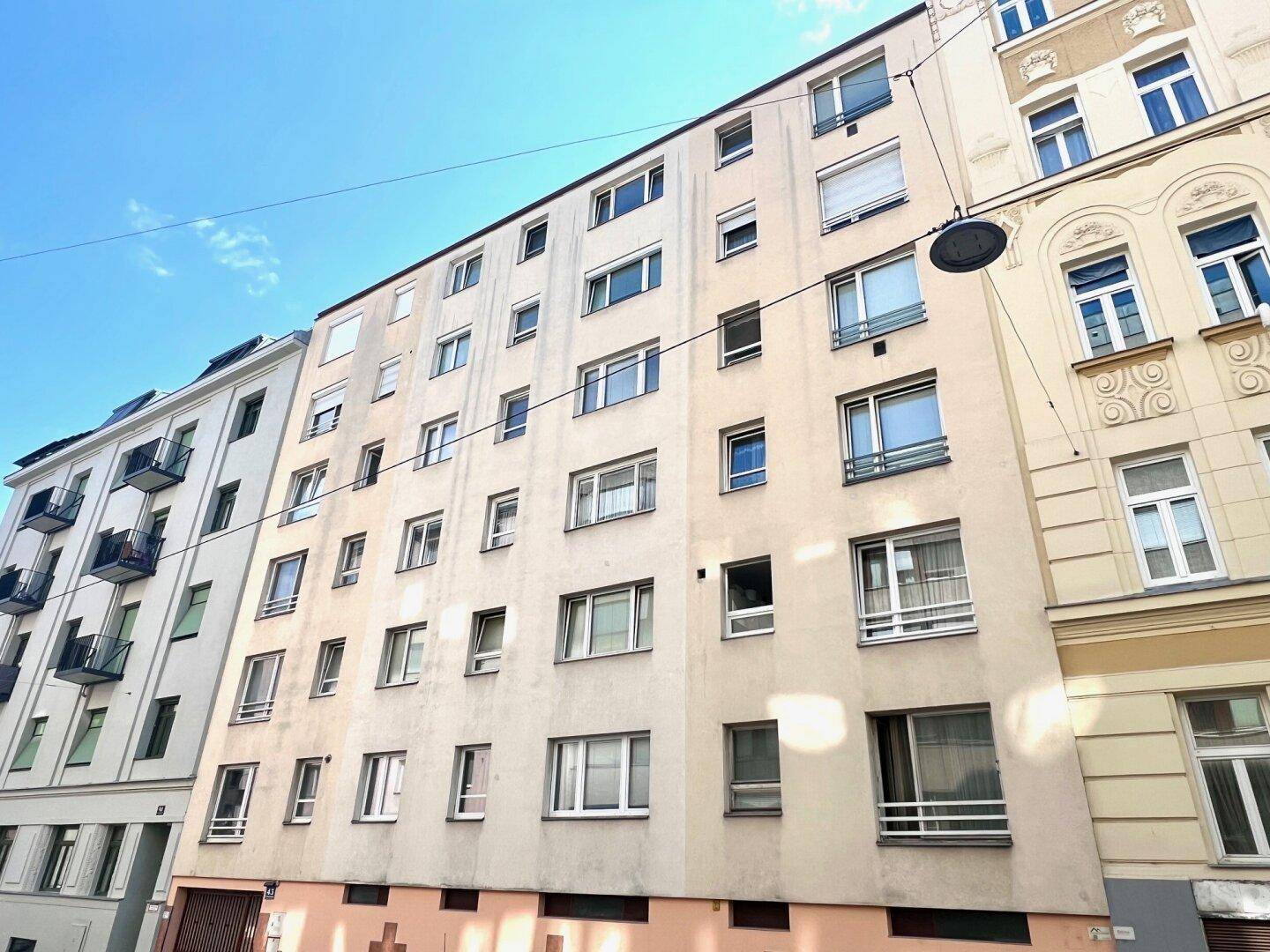 Mehrstöckiges Wohngebäude mit zahlreichen Fenstern und einer hellen Fassade in städtischer Umgebung.