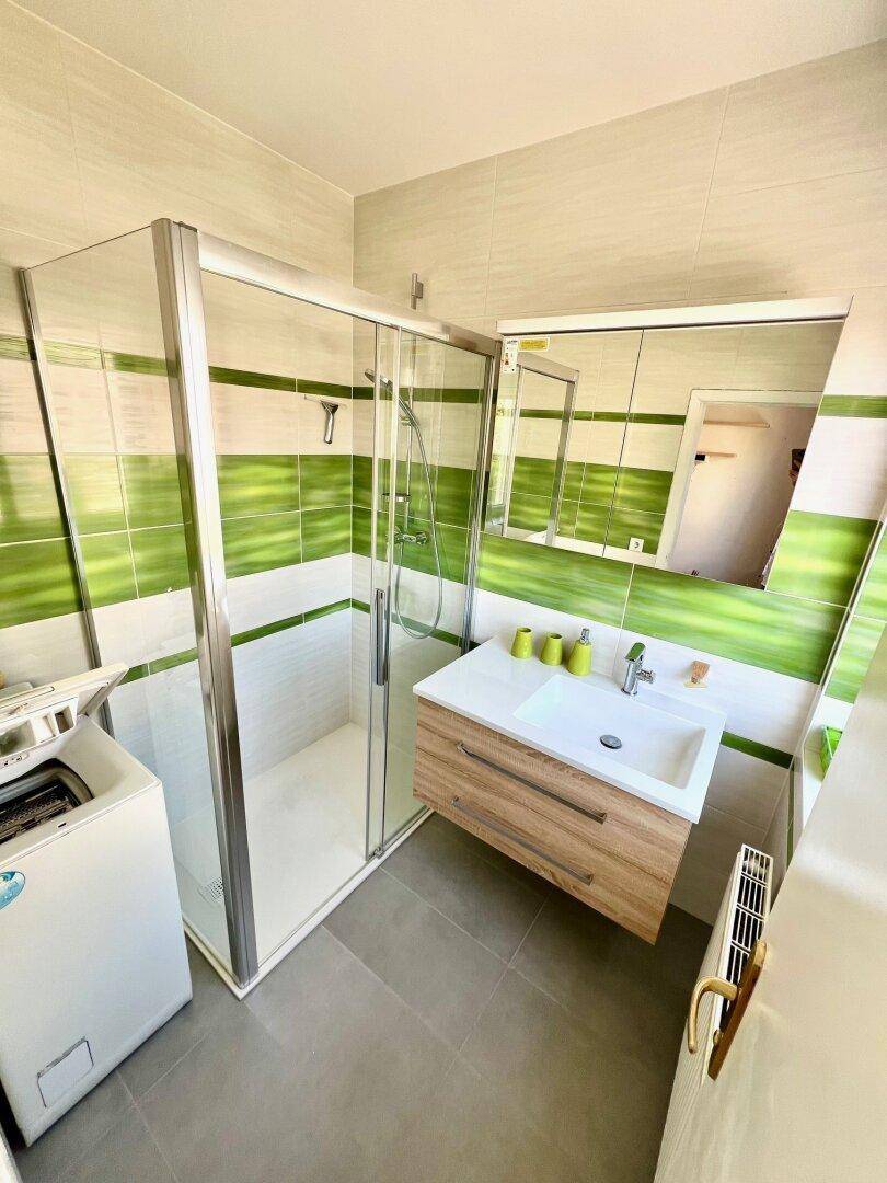 Modernes Badezimmer mit grünen Akzentfliesen, Duschkabine und Waschmaschinenanschluss.