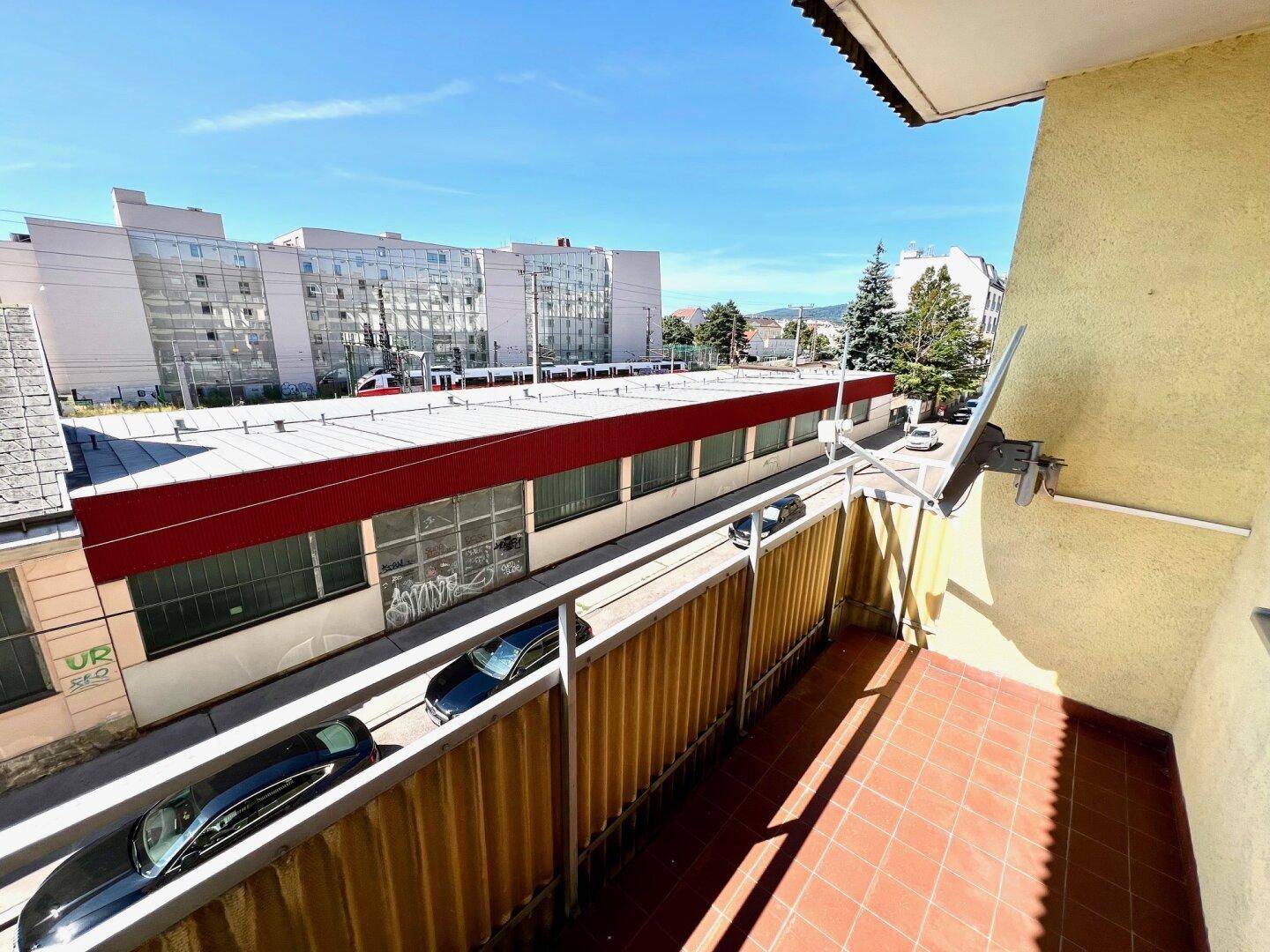 Balkon mit Fliesenboden und Blick auf die umliegende Stadtbebauung und Straße.