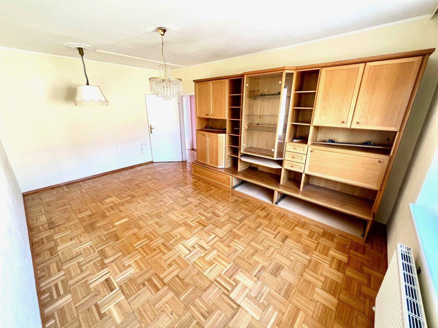 Geräumiges Wohnzimmer mit Parkettboden und einer umfangreichen Holzschrankwand.