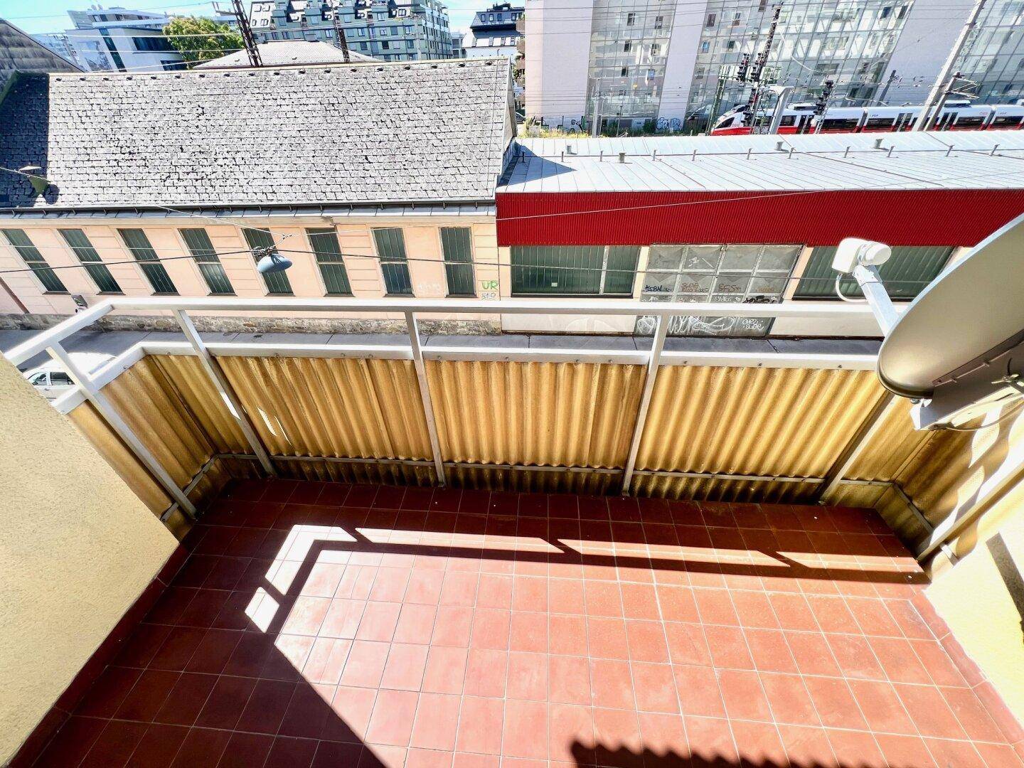 Geräumiger Balkon mit Terrakottafliesen und Blick auf die Dächer der Nachbargebäude.