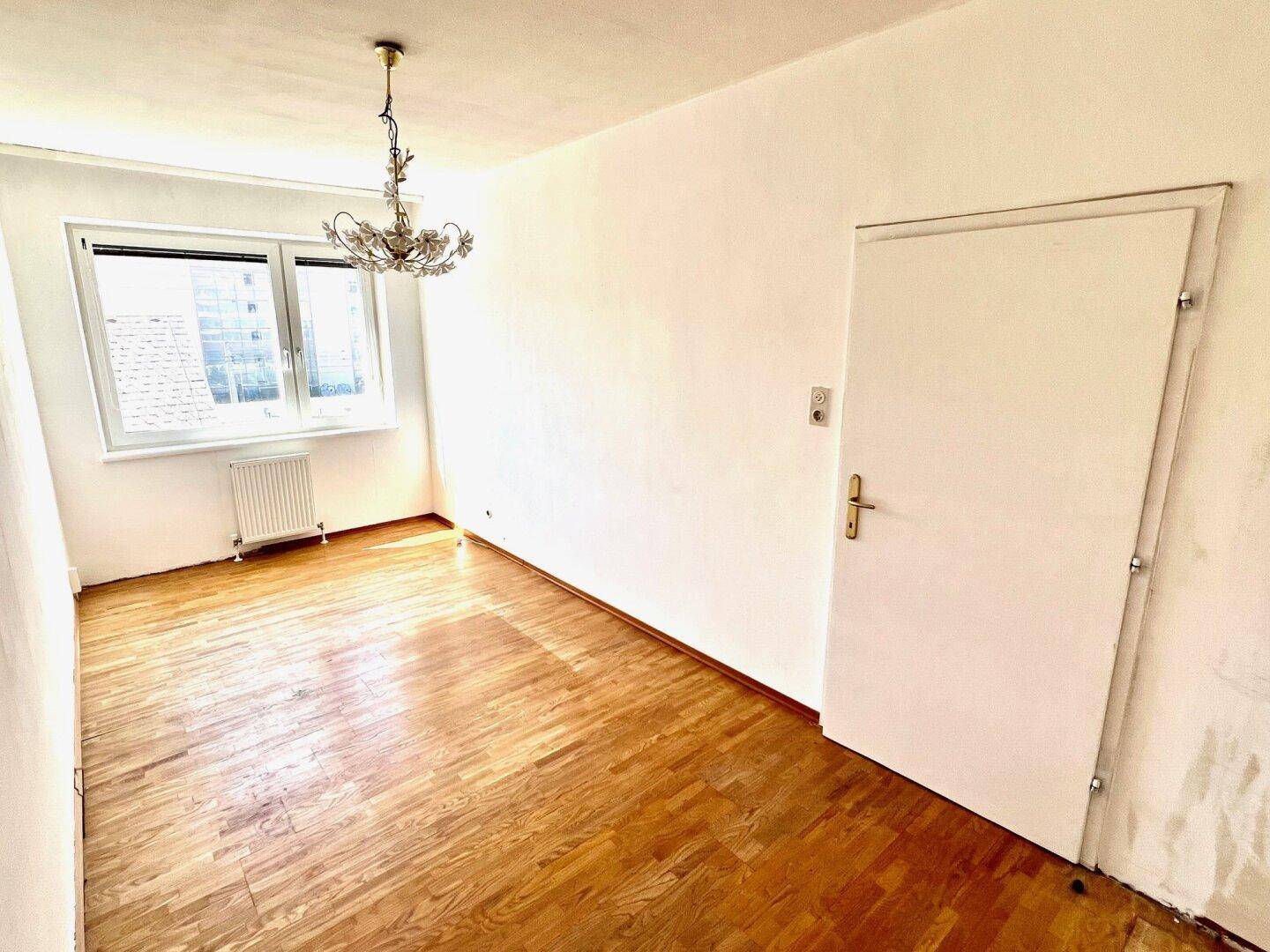 Leeres Zimmer mit Parkettboden und Fenster, bereit zur individuellen Gestaltung.